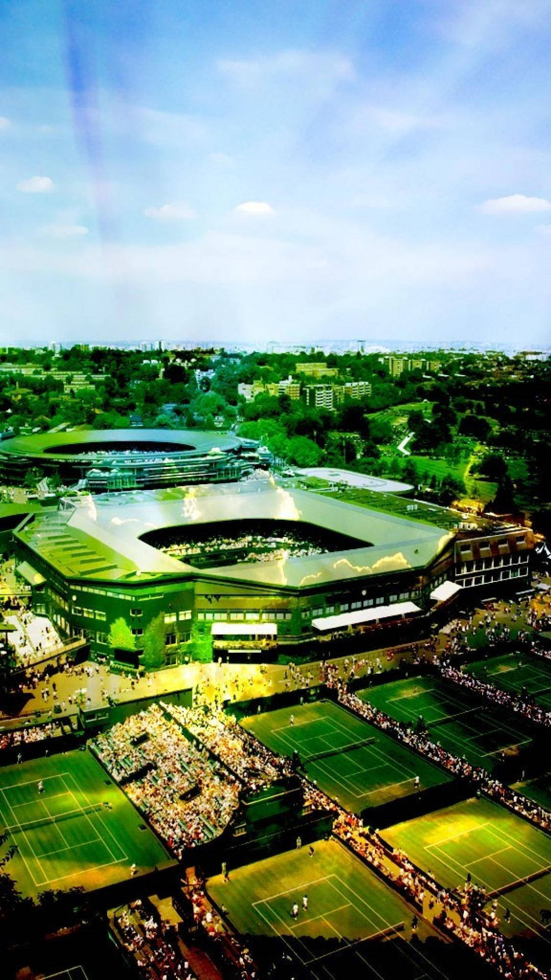 Wimbledon 桌布 壁紙 — 鳥瞰一個宏偉的網球綜合體，多個球場在明亮的藍天下擠滿了觀眾。