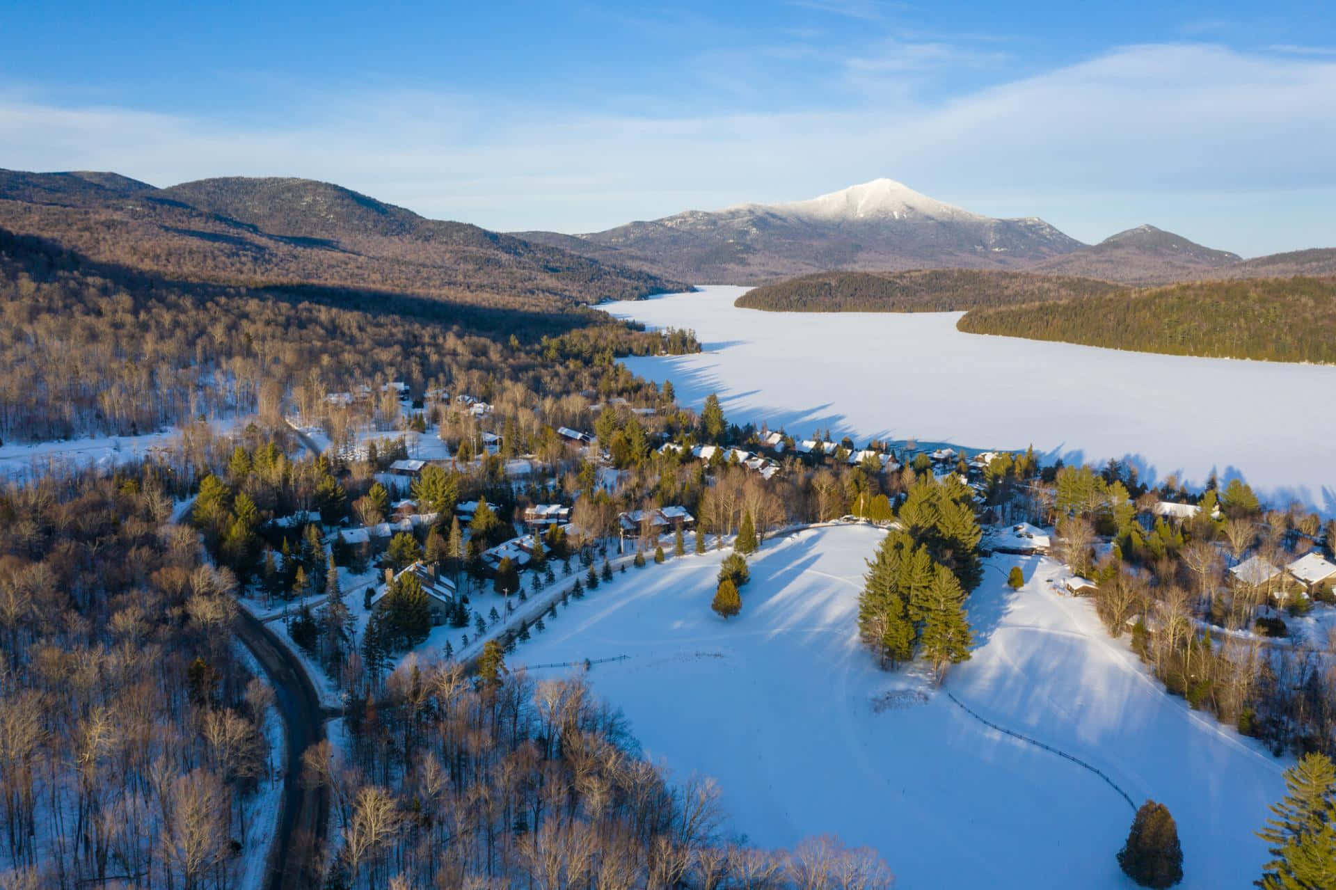 Lake 桌布 壁紙 — 鳥瞰一個被雪覆蓋的村莊，坐落在結冰的湖邊，遠處有積雪的山峰，在清澈的藍天下。