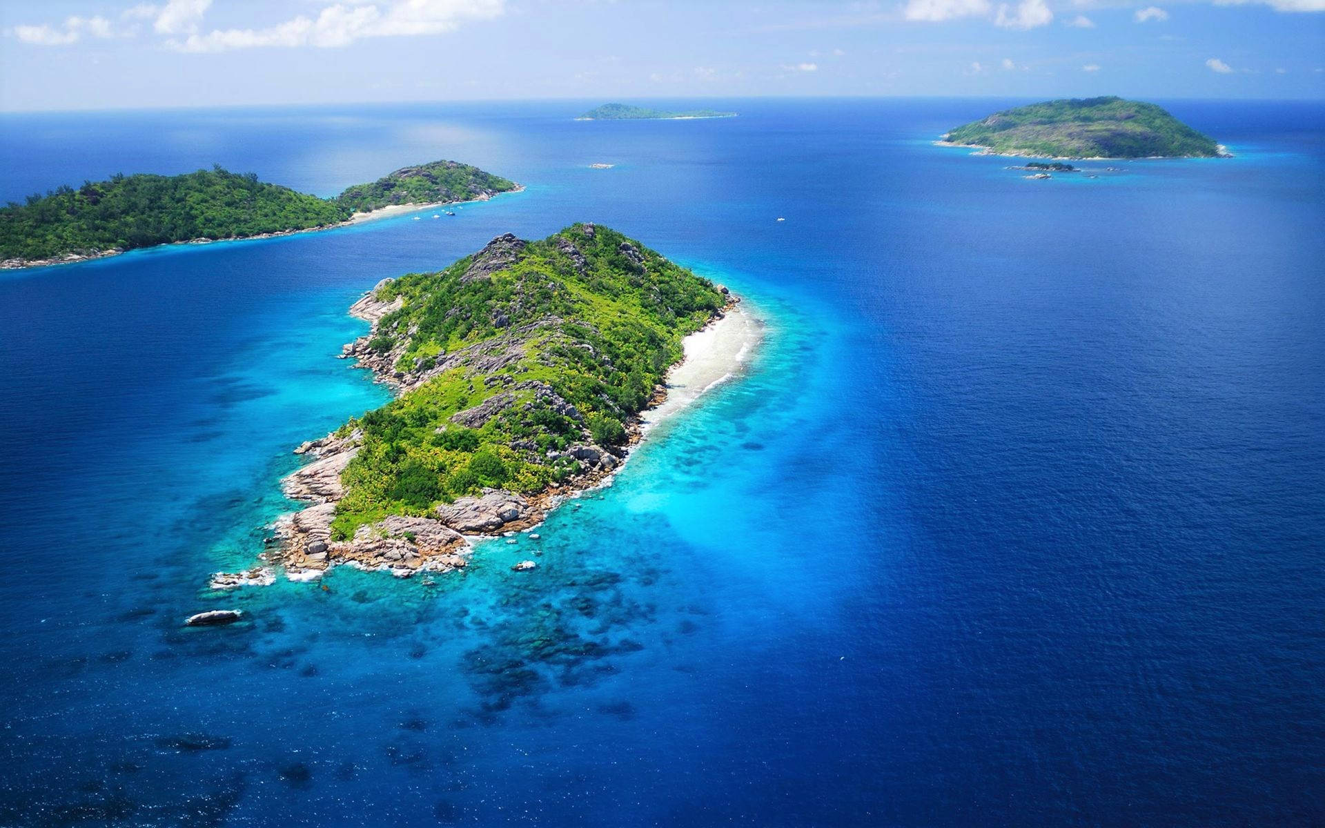 Seychelles 桌布 壁紙 — 鳥瞰一個鬱鬱蔥蔥的綠色島嶼，擁有白色沙灘，周圍環繞著充滿活力的碧綠和深藍色海水。