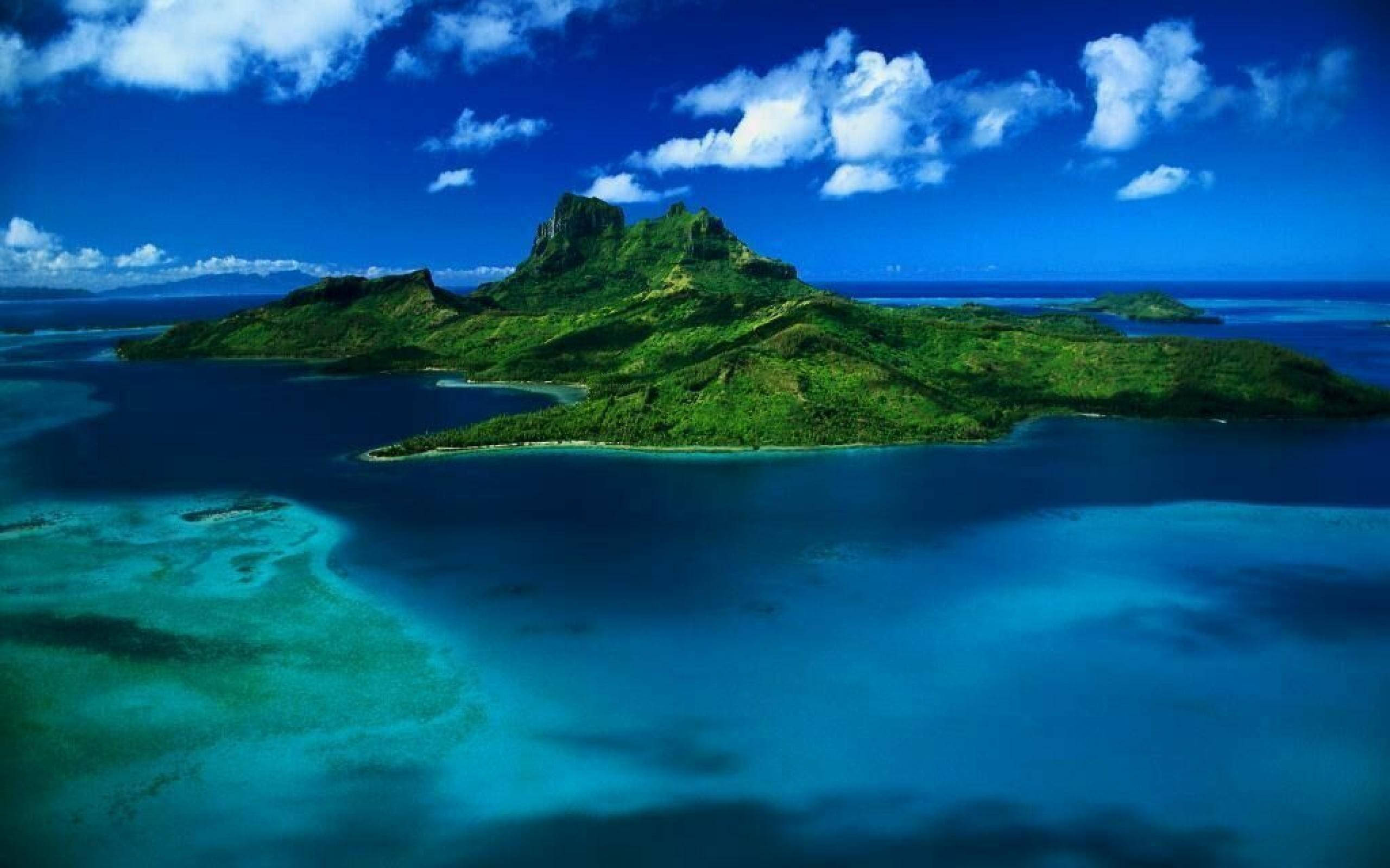 Philippines 桌布 壁紙 — 鳥瞰一個鬱鬱蔥蔥的綠色火山島，周圍環繞著充滿活力的綠松石潟湖和深藍色海洋，在明亮的天空下，有蓬鬆的白雲。