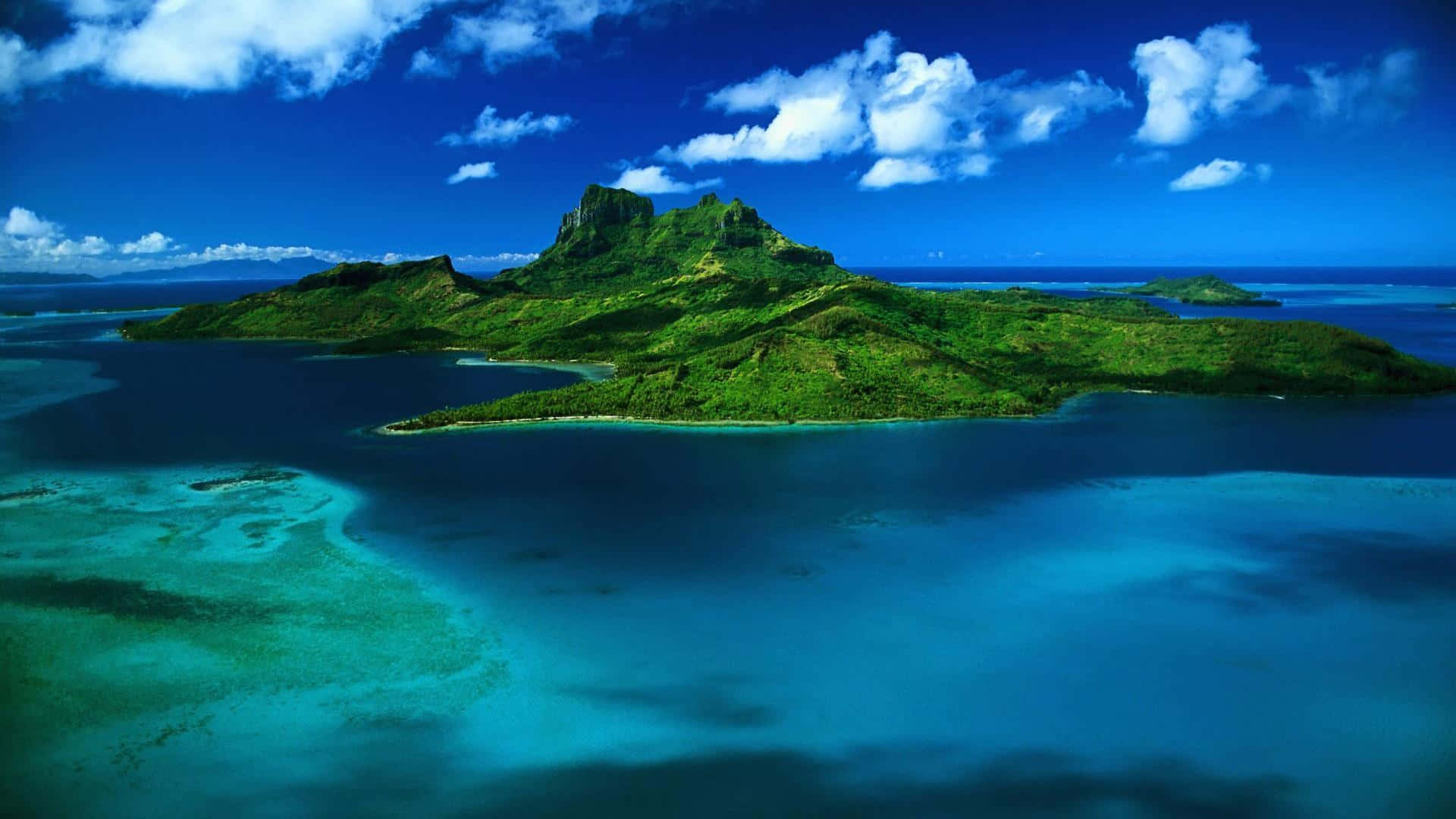 Cool Nature 桌布 壁紙 — 鳥瞰一個鬱鬱蔥蔥的綠色火山島，周圍環繞著充滿活力的綠松石色潟湖，在明亮的藍天下有蓬鬆的白雲。