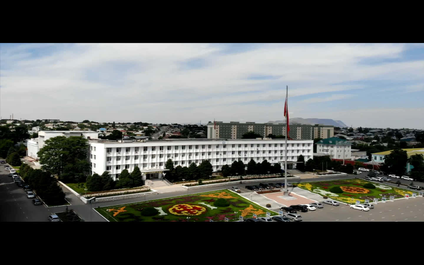 Building 桌布 壁紙 — 鳥瞰一座大型白色政府建築，擁有修剪整齊的花壇和一根高高的旗杆，天空多雲。