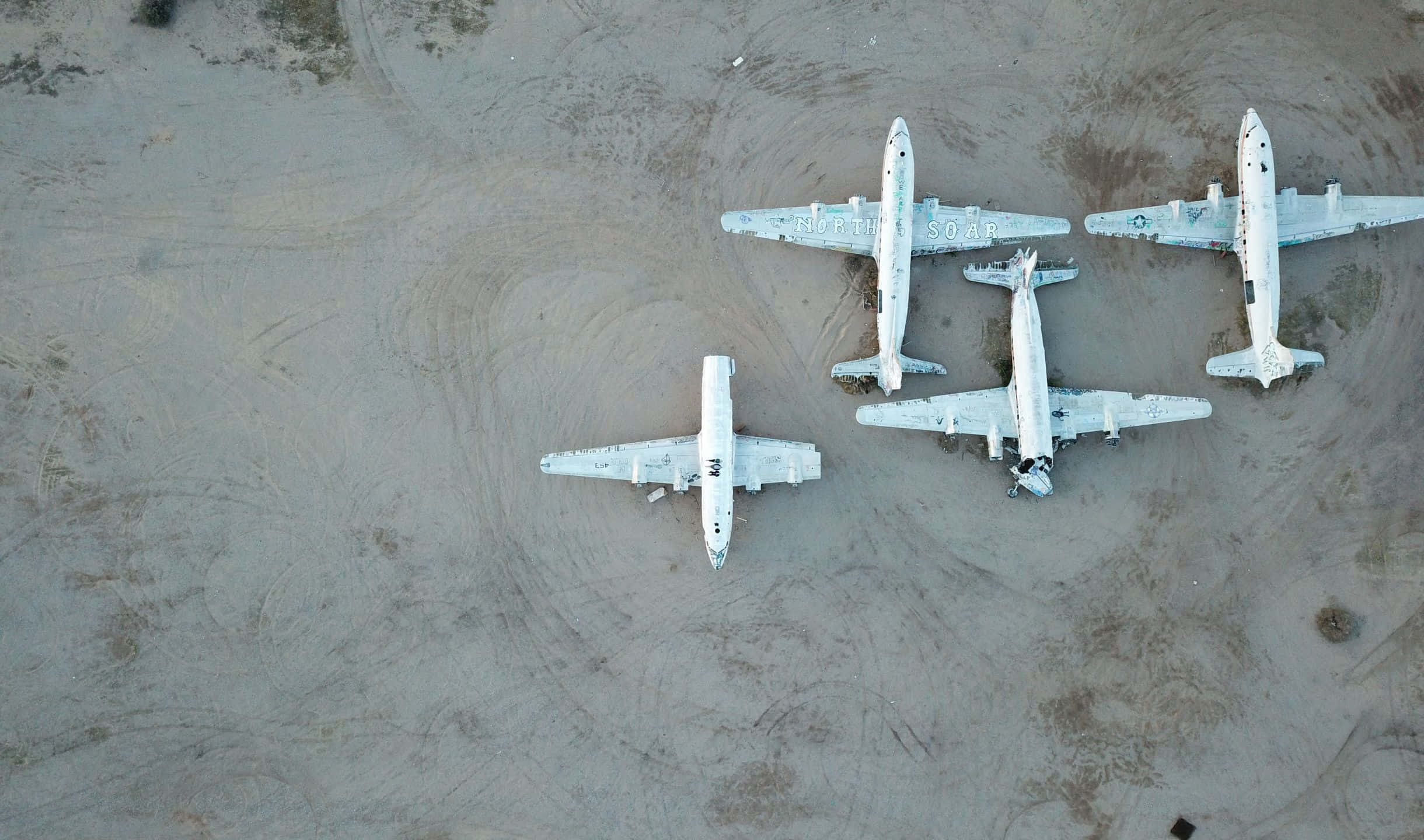 2440x1440 Small Planes 桌布 壁紙 — 鳥瞰四架白色復古飛機停泊在廣闊的沙質沙漠地面上。
