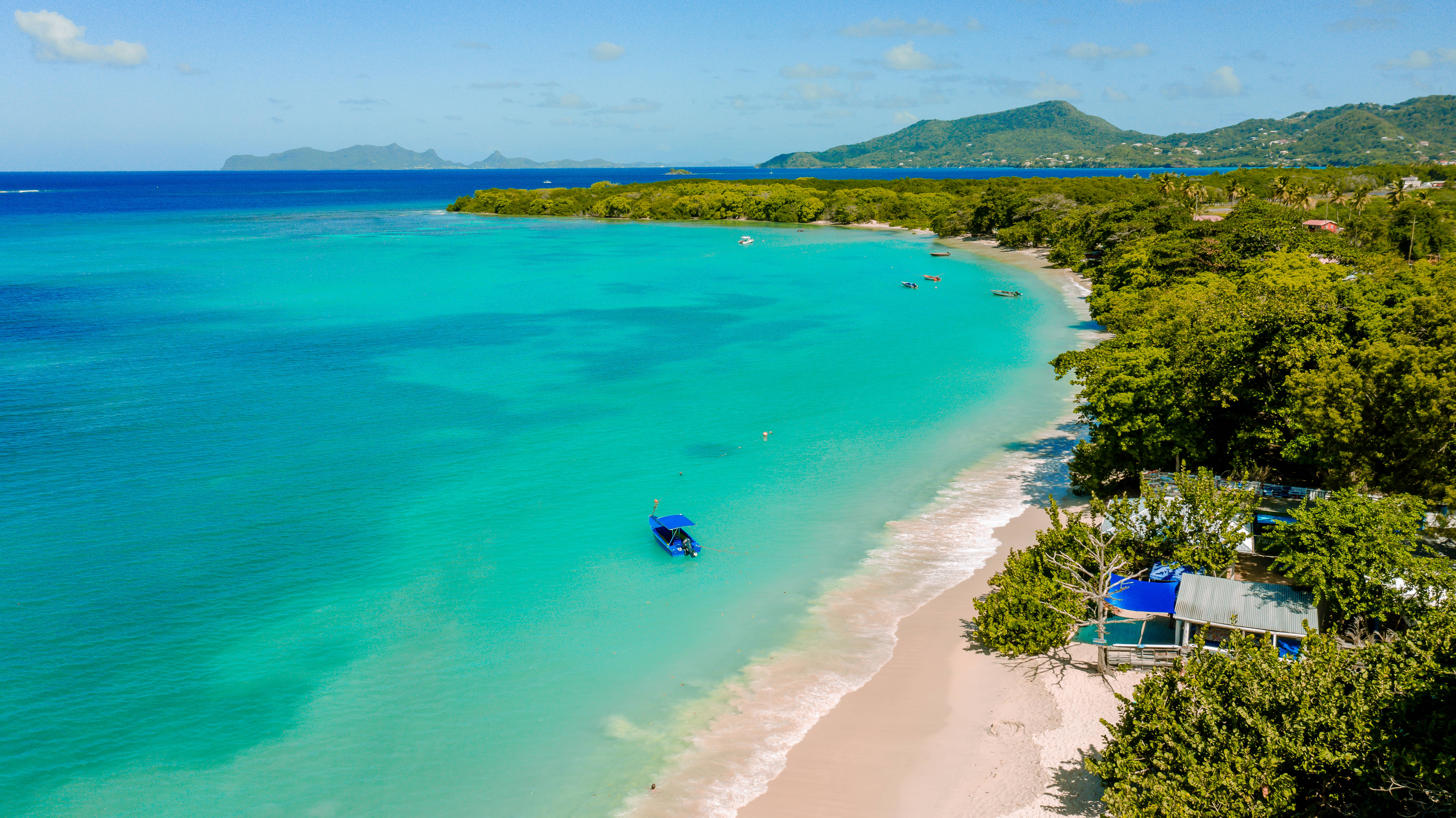 Grenada 桌布 壁紙 — 鳥瞰圖：一個藍綠色潟湖，一艘藍色小船在白色沙灘附近漂流，沙灘兩旁長滿茂密的綠樹。