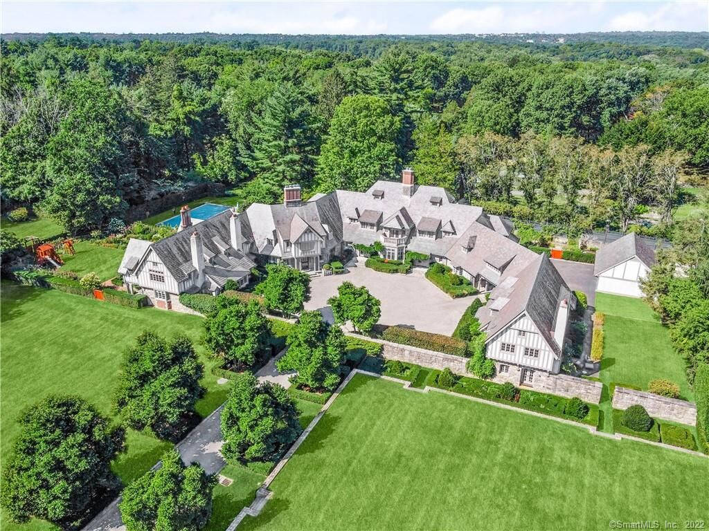Mansion 桌布 壁紙 — 鳥瞰圖：一座宏偉的都鐸式大宅，四周環繞著茂密的綠色草坪和茂密森林，在明亮的日光下。