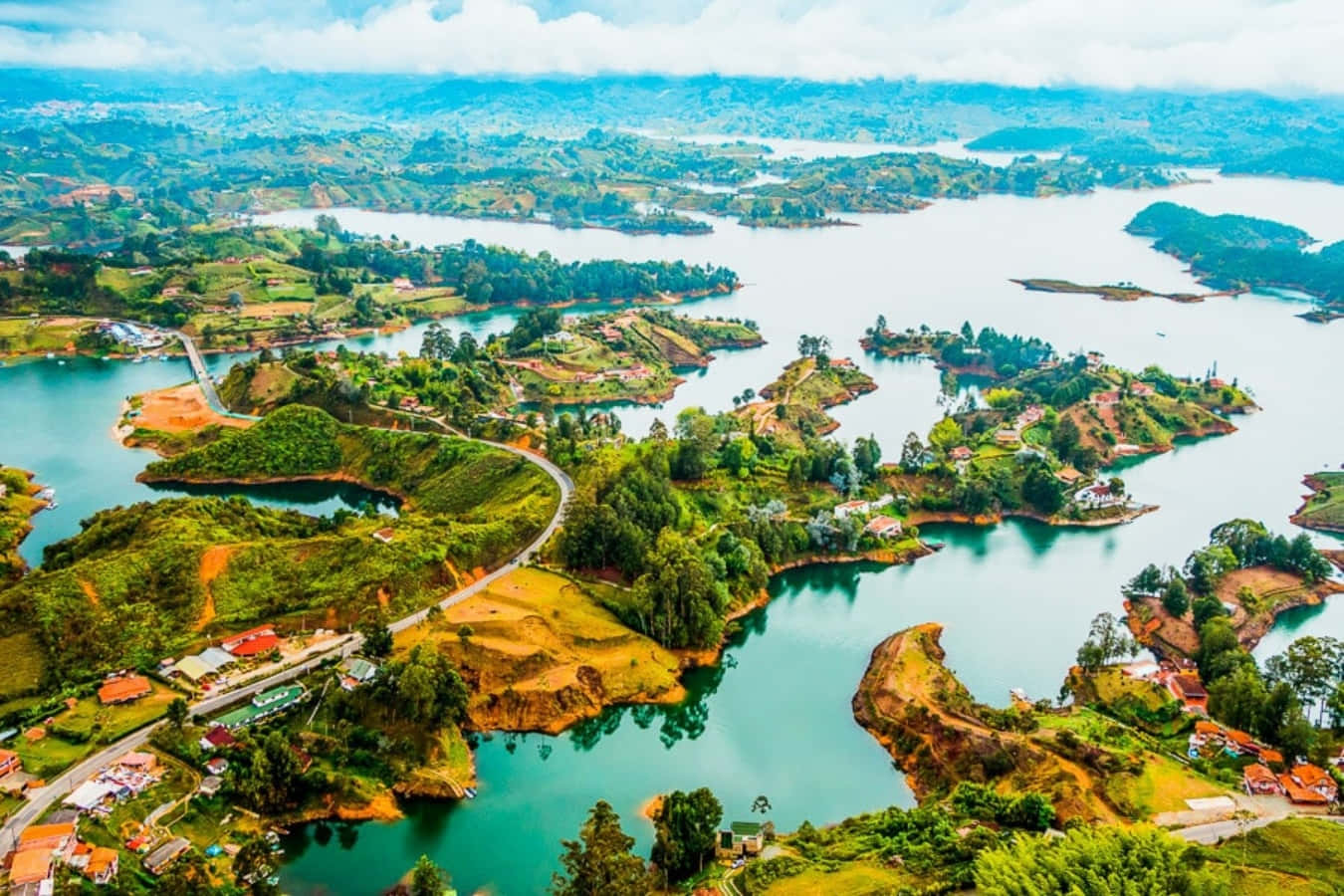 Colombia 桌布 壁紙 — 鳥瞰圖，一條蜿蜒的道路環繞著碧綠的湖泊和鬱鬱蔥蔥的綠色島嶼，島上點綴著小房子，天空多雲。