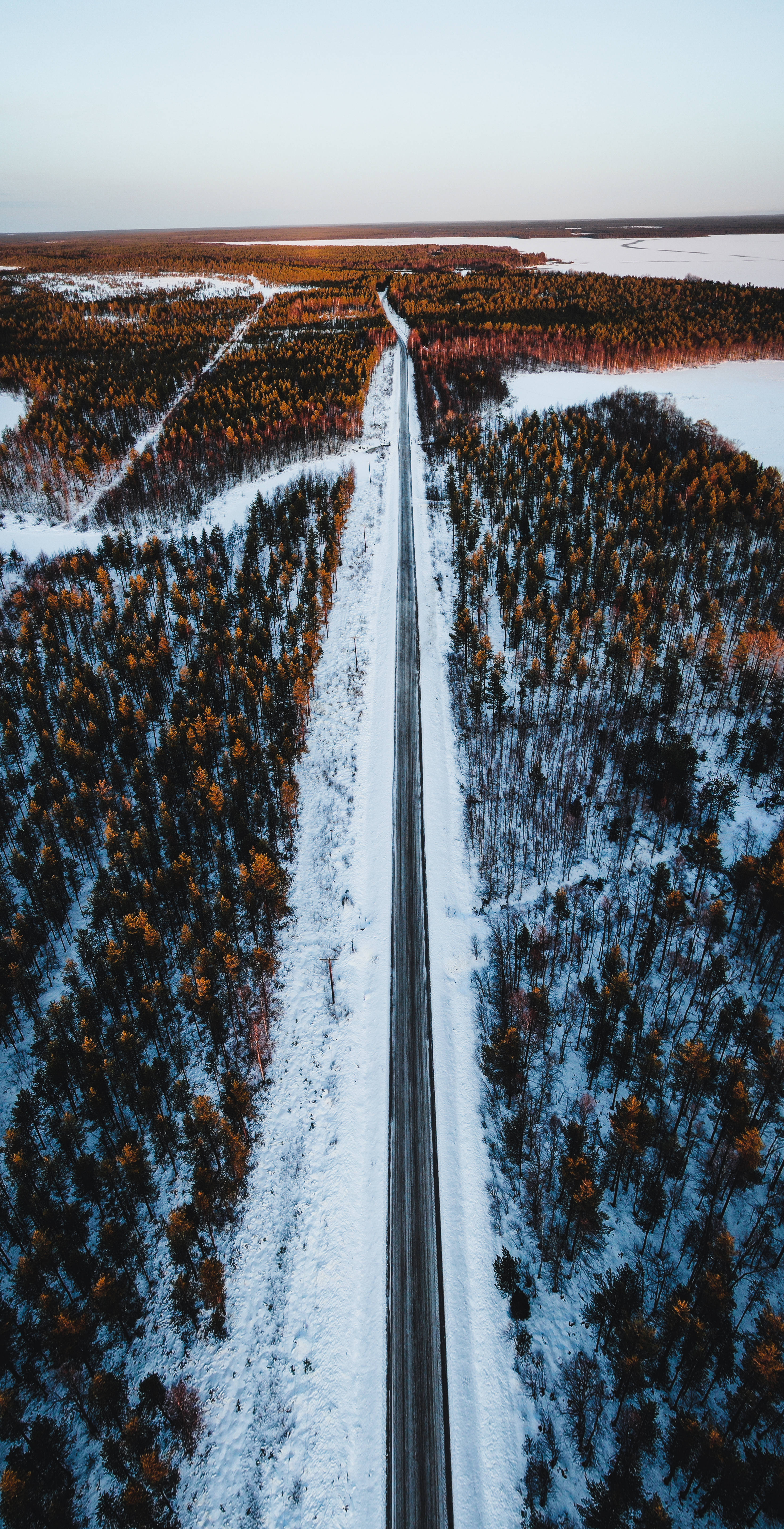 Finland 桌布 壁紙 — 鳥瞰圖：一條被雪覆蓋的道路在日落時分穿過冰凍的森林，呈現橙色和藍色色調。