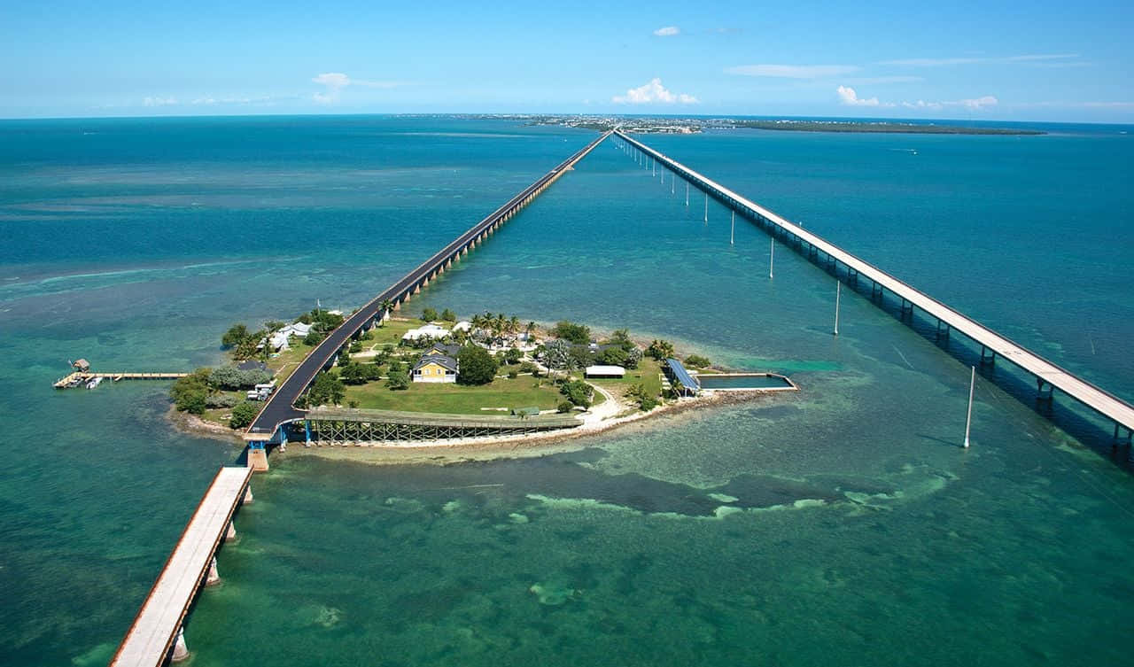 Key West 桌布 壁紙 — 鳥瞰圖：一條長橋橫跨碧綠海水，通往一個有房屋和棕櫚樹的小島，天空清澈湛藍。