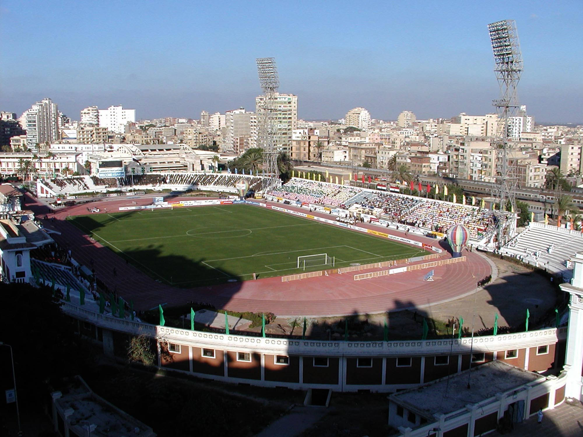 Alexandria 桌布 壁紙 — 鳥瞰圖：一片充滿活力的綠色足球場，被紅色跑道和擠滿觀眾的看台環繞，上方是清澈的藍天。