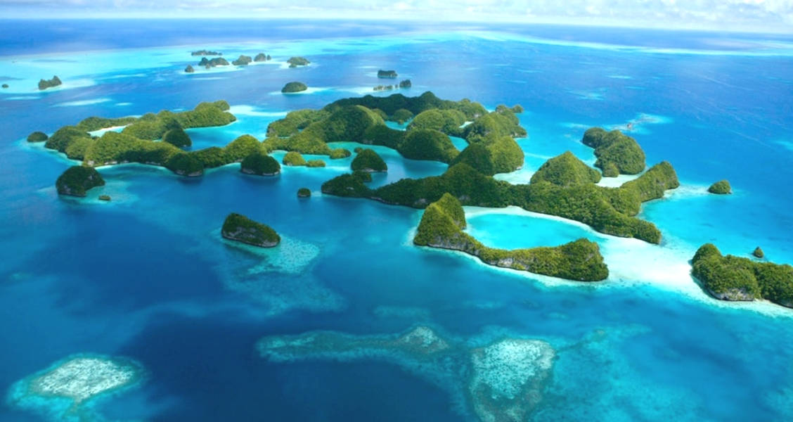 Micronesia 桌布 壁紙 — 鳥瞰圖：在明亮的日光下，鬱鬱蔥蔥的綠色島嶼散落在充滿活力的碧綠和深藍色海洋水域中。