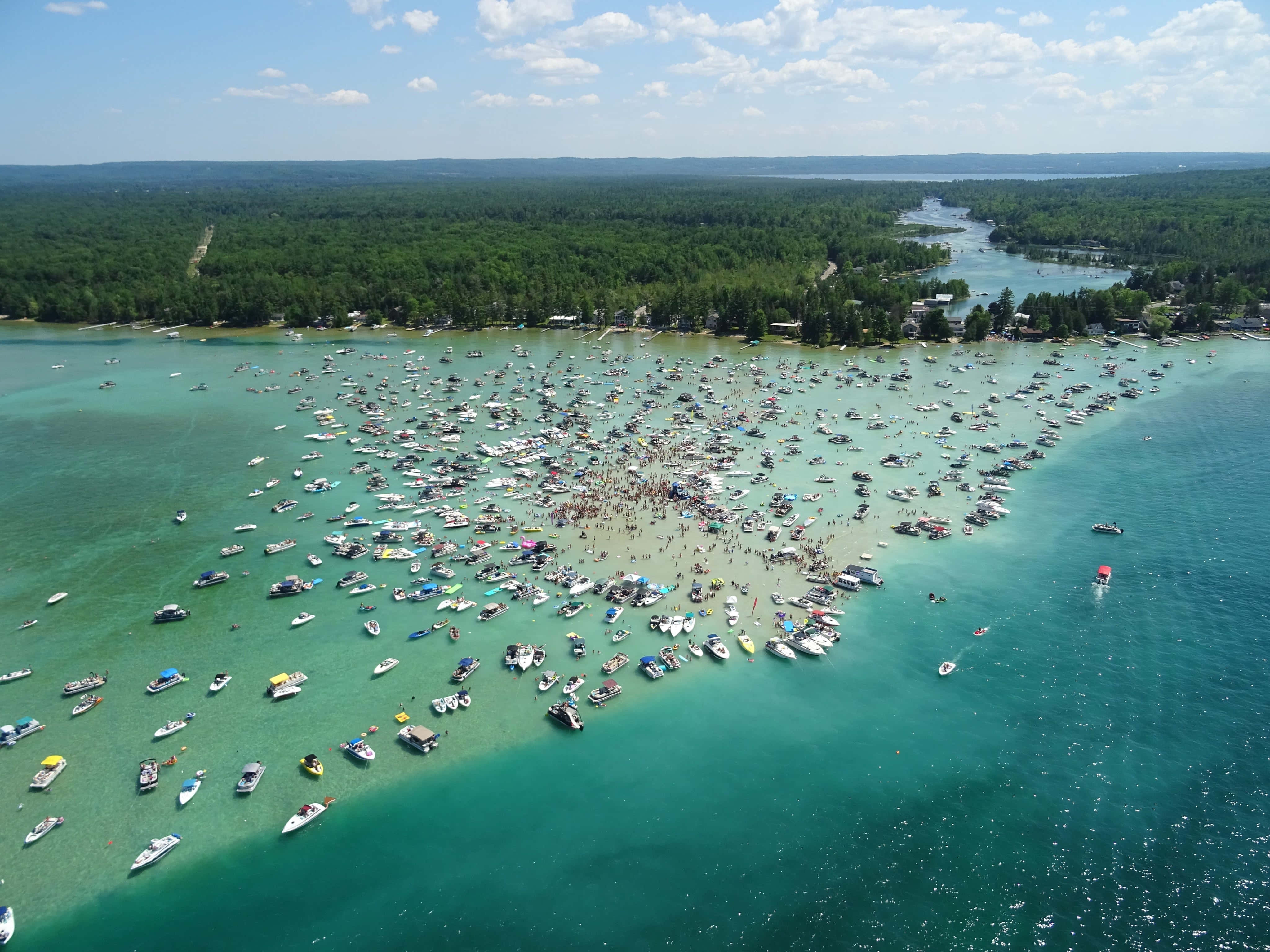 Torch Lake 桌布 壁紙 — 鳥瞰圖：在明亮的藍天下，數百艘船隻和人群聚集在淺沙洲上，擠滿了碧綠色的湖泊。
