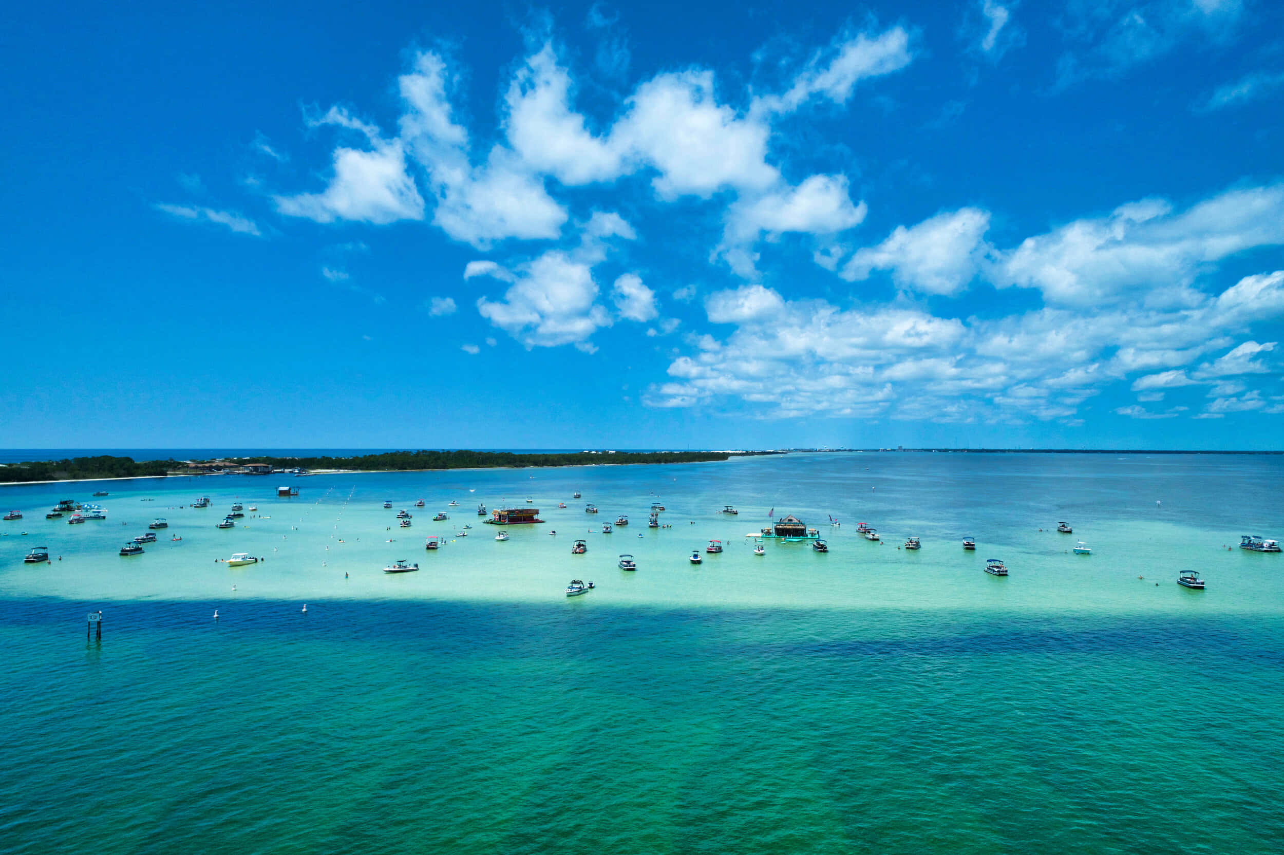 Crab Island 桌布 壁紙 — 鳥瞰圖：在明亮的藍天和蓬鬆的白雲下，點綴著船隻的碧綠海水。