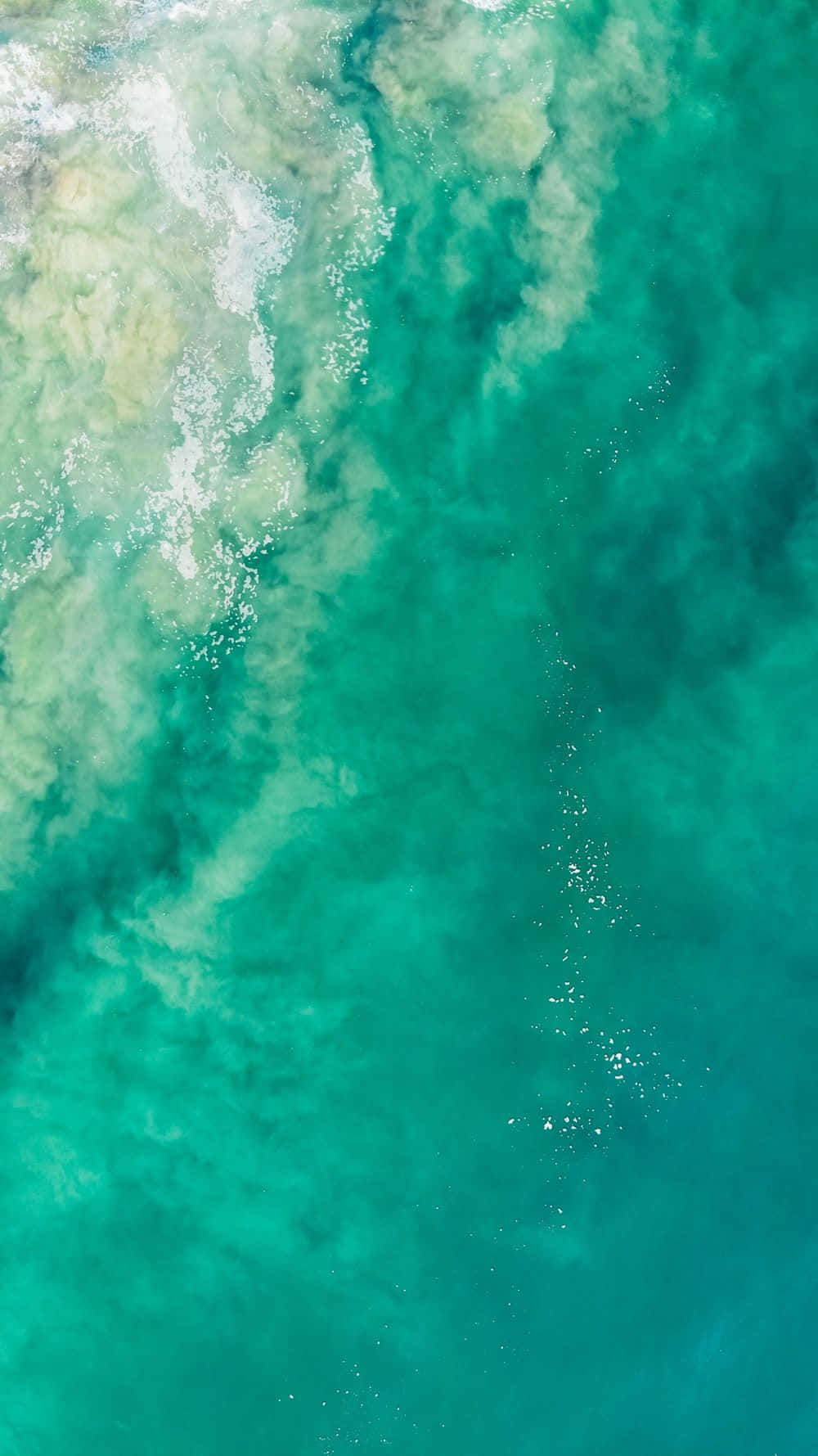 Turquoise iPhone 桌布 壁紙 — 鳥瞰圖：帶有白色泡沫和綠色底色的碧綠海水翻騰。