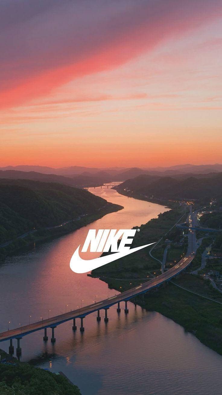 Nike iPhone 桌布 壁紙 — 鳥瞰圖：日落時分蜿蜒的河流，橋樑和道路在粉橙色天空下閃耀，並疊加Nike標誌。