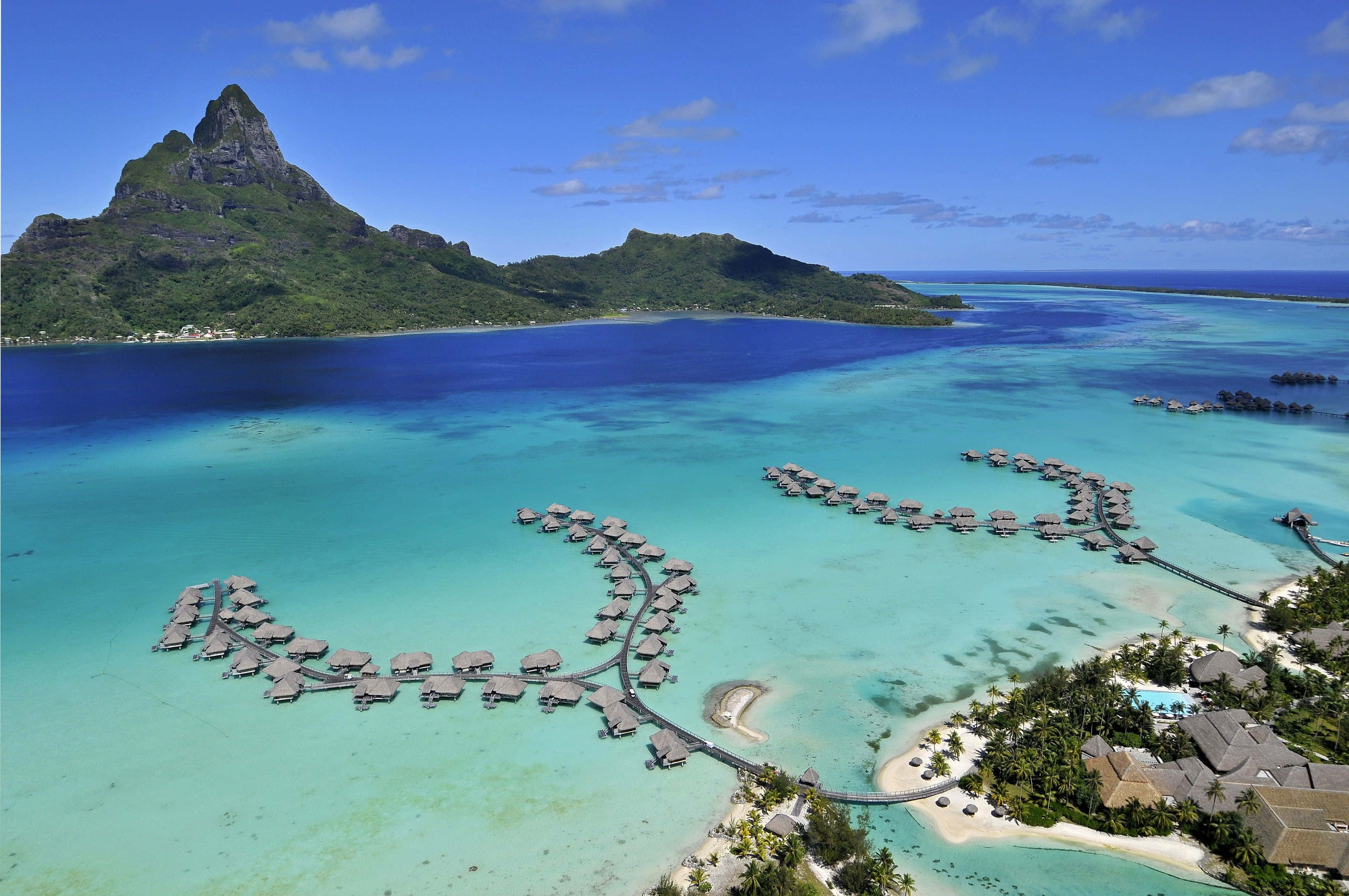 Bora Bora 桌布 壁紙 — 鳥瞰圖：水上平房蜿蜒穿過碧綠潟湖，旁邊是鬱鬱蔥蔥的青山，天空清澈湛藍。