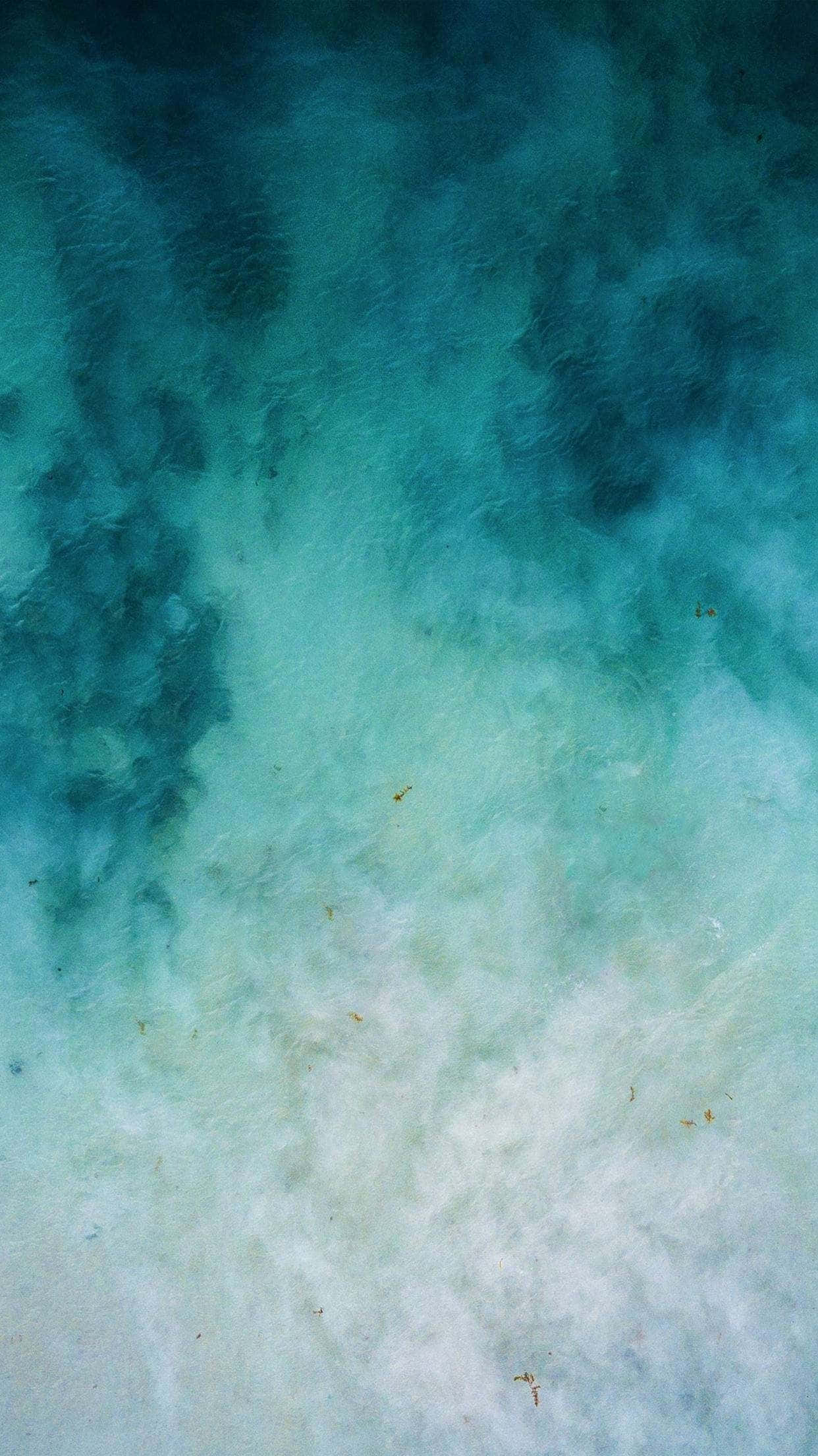 Blue Watercolor 桌布 壁紙 — 鳥瞰圖：碧綠海水在沙質海床上旋轉，散落著海藻。
