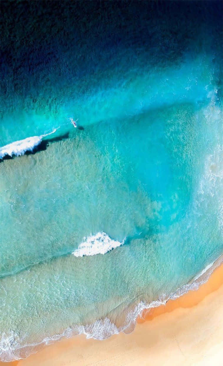 Turquoise iPhone 桌布 壁紙 — 鳥瞰圖：碧綠海浪輕輕拍打金色沙灘，一名孤獨的衝浪者正在乘風破浪。