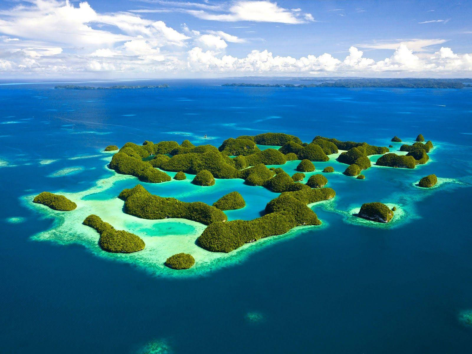 Palau 桌布 壁紙 — 鳥瞰圖：鬱鬱蔥蔥的綠色島嶼被充滿活力的碧綠和深藍色海洋環繞，天空明亮，雲朵蓬鬆。