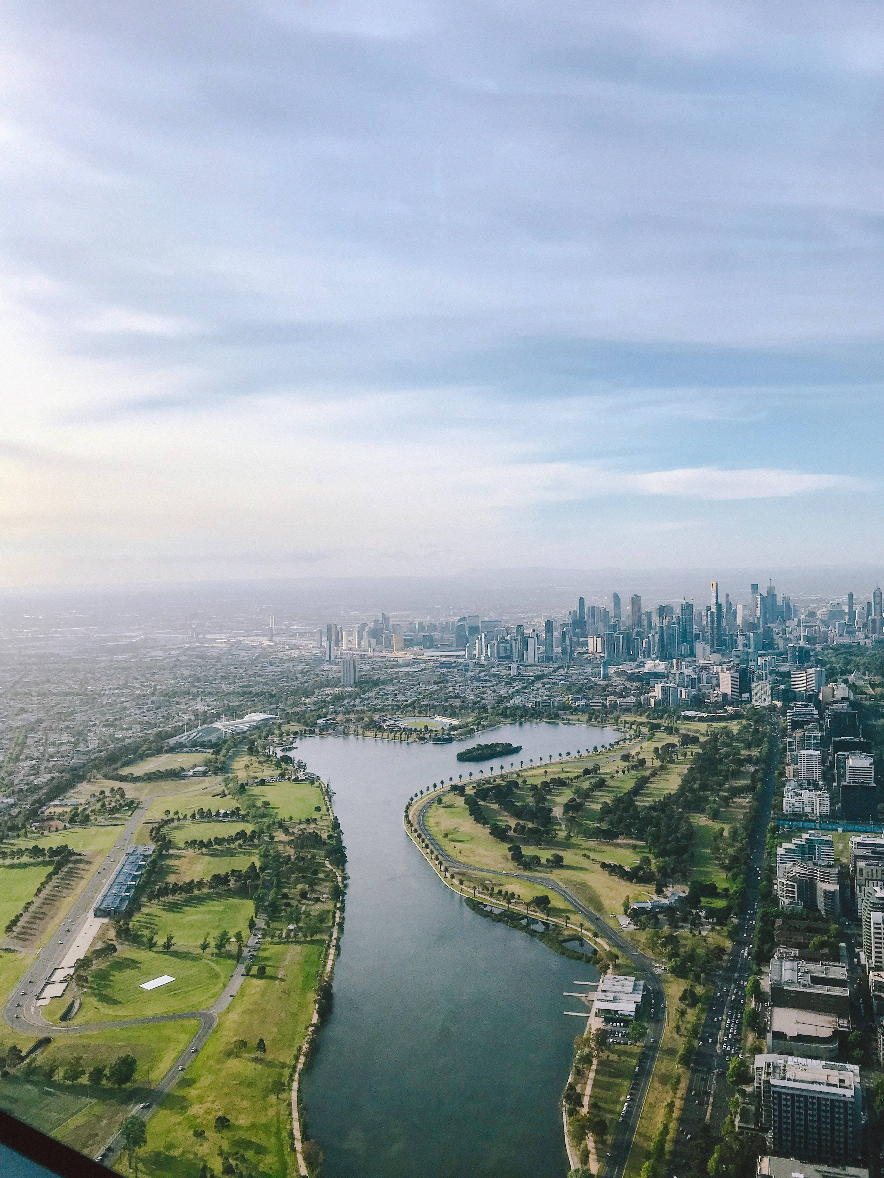 river 桌布 壁紙 — 鳥瞰圖顯示一個廣闊的城市景觀，有一條蜿蜒的河流，兩旁是茂密的綠色公園，在柔和的藍天下。