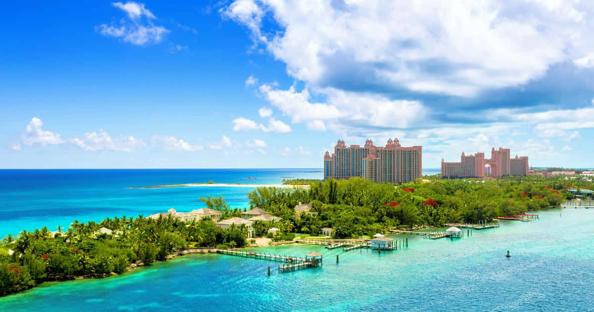 Bahamas Island 桌布 壁紙 — 鳥瞰圖顯示一個豪華度假村，粉紅色塔樓坐落在鬱鬱蔥蔥的綠植中，旁邊是碧綠的海水，上方是明亮的藍天和蓬鬆的白雲。