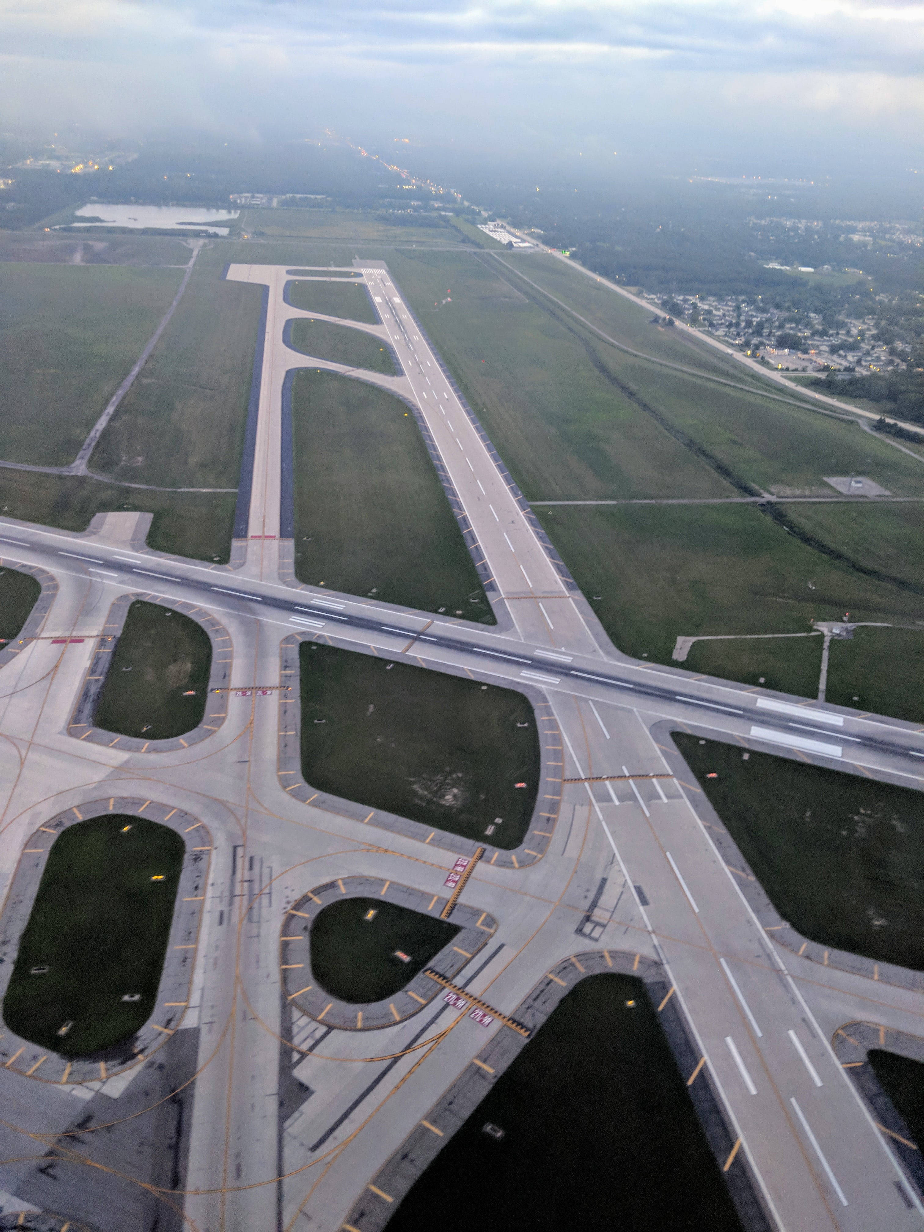 Runway 桌布 壁紙 — 鳥瞰圖顯示一條廣闊的機場跑道和滑行道，與道路和綠色田野交錯，天空多雲。