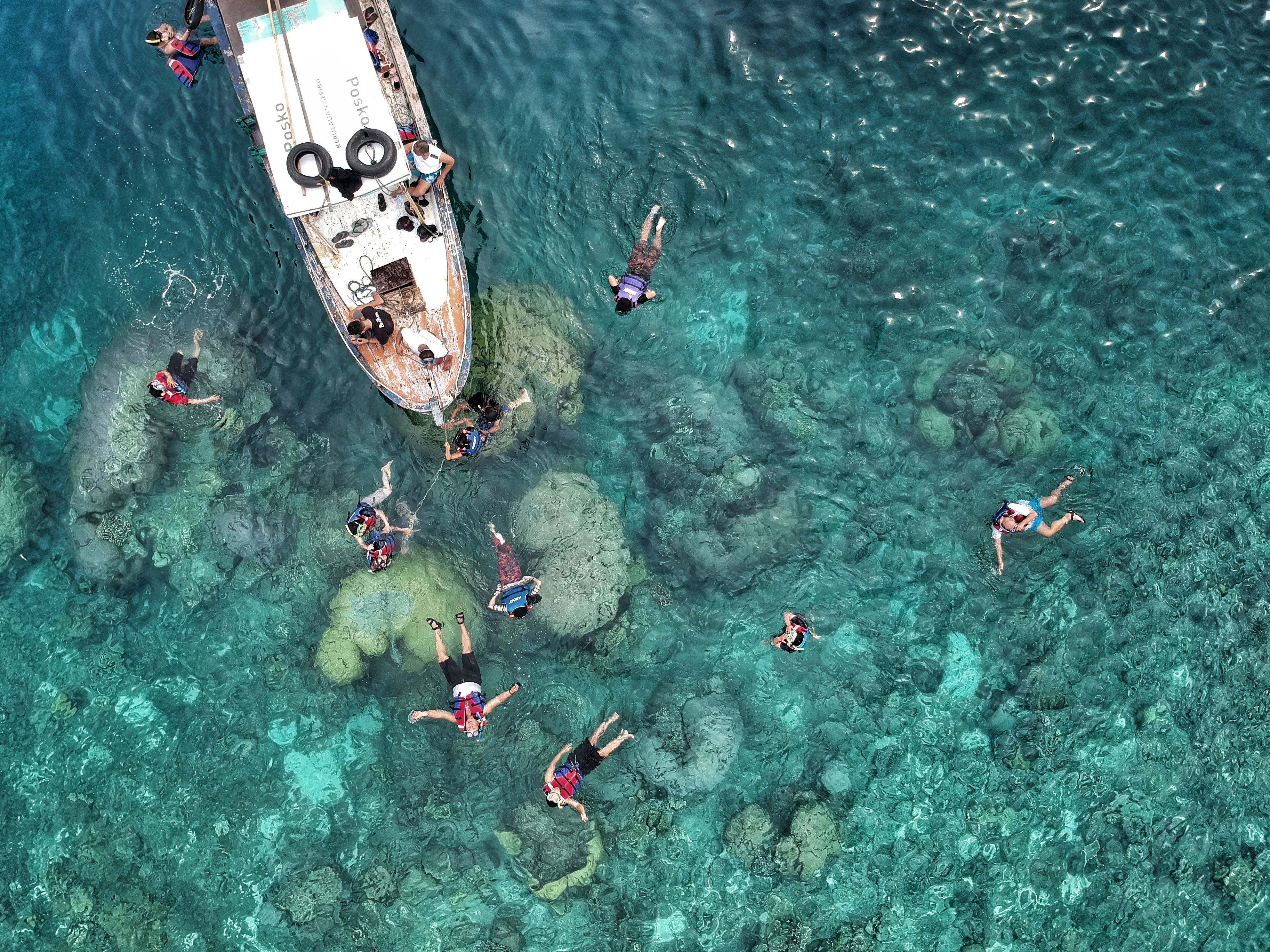 Snorkeling 桌布 壁紙 — 鳥瞰圖顯示人們在清澈碧綠的海水中漂浮和游泳，附近有一艘小船錨泊在珊瑚礁上。