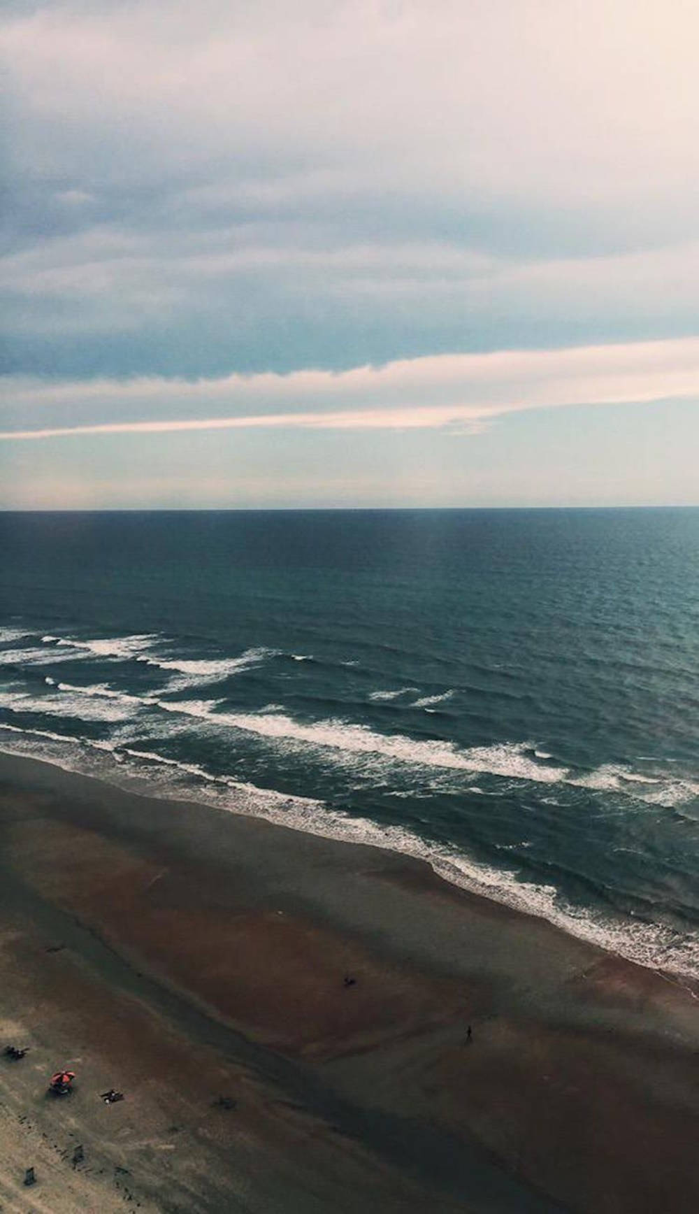 Ocean iPhone 桌布 壁紙 — 鳥瞰廣闊海洋與沙灘相接，天空多雲，溫柔海浪緩緩拍岸。