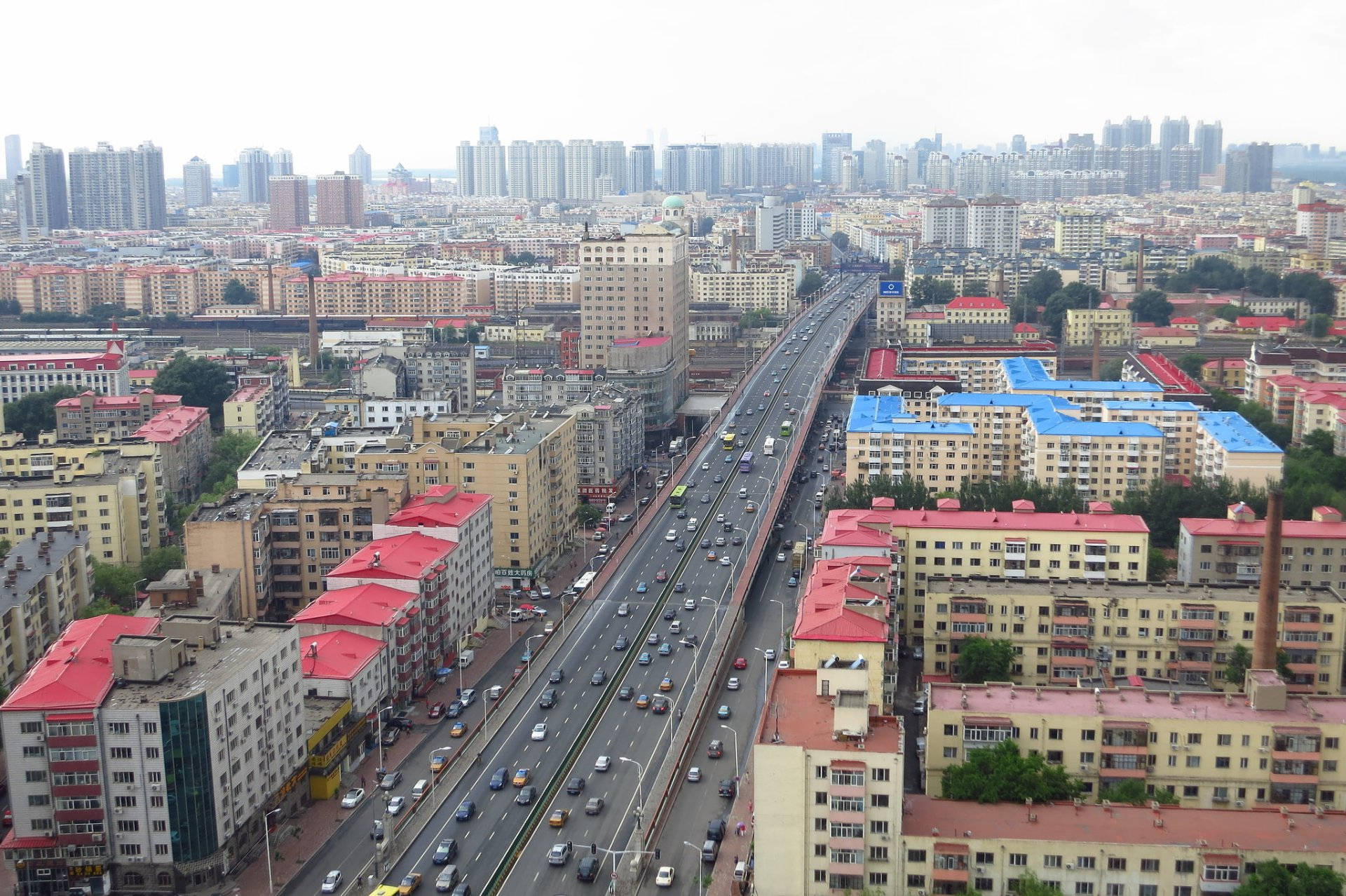 Harbin 桌布 壁紙 — 鳥瞰繁忙的城市景觀，多車道高速公路穿過密集的住宅建築，天空多雲。
