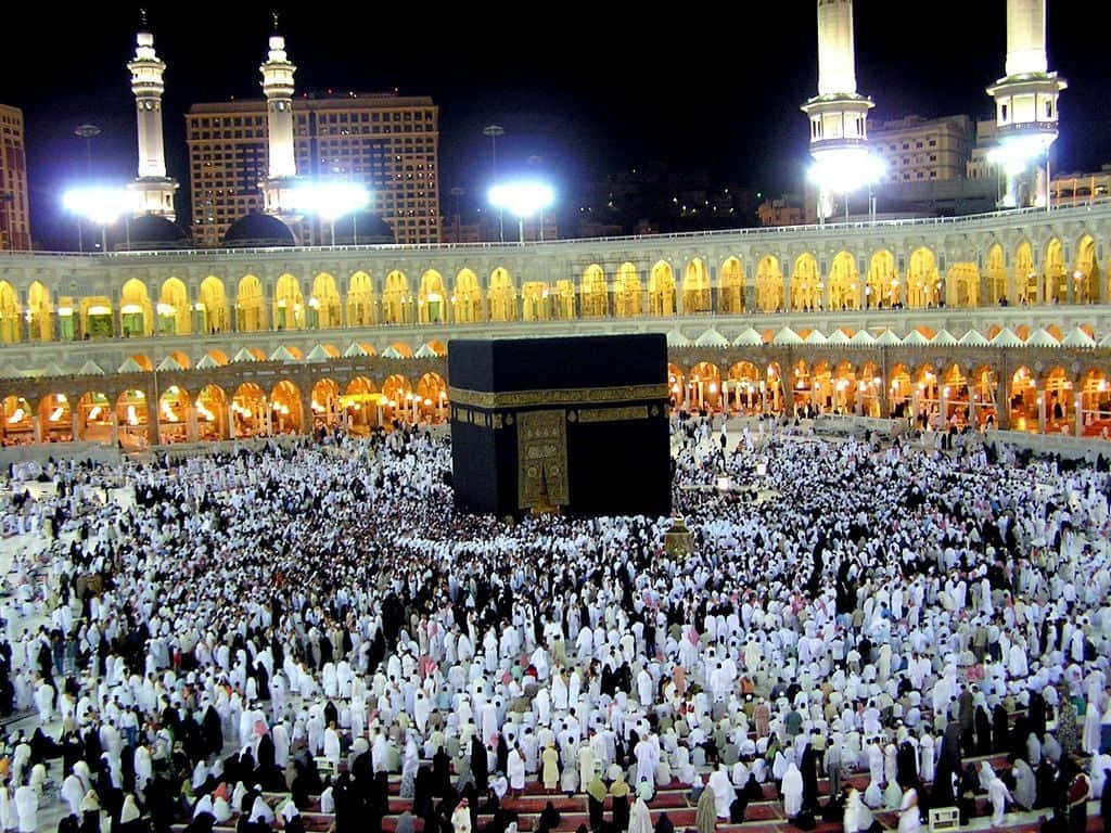 Makkah 桌布 壁紙 — 麥加天房的夜景，數百萬身穿白衣的朝聖者在明亮燈光下環繞。