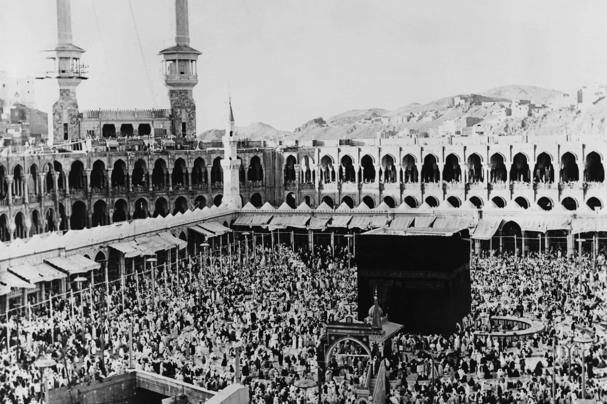 Mecca Mosque 桌布 壁紙 — 麥加禁寺內，拱形柱廊和宣禮塔下，大批人群圍繞卡巴天房的黑白照片。