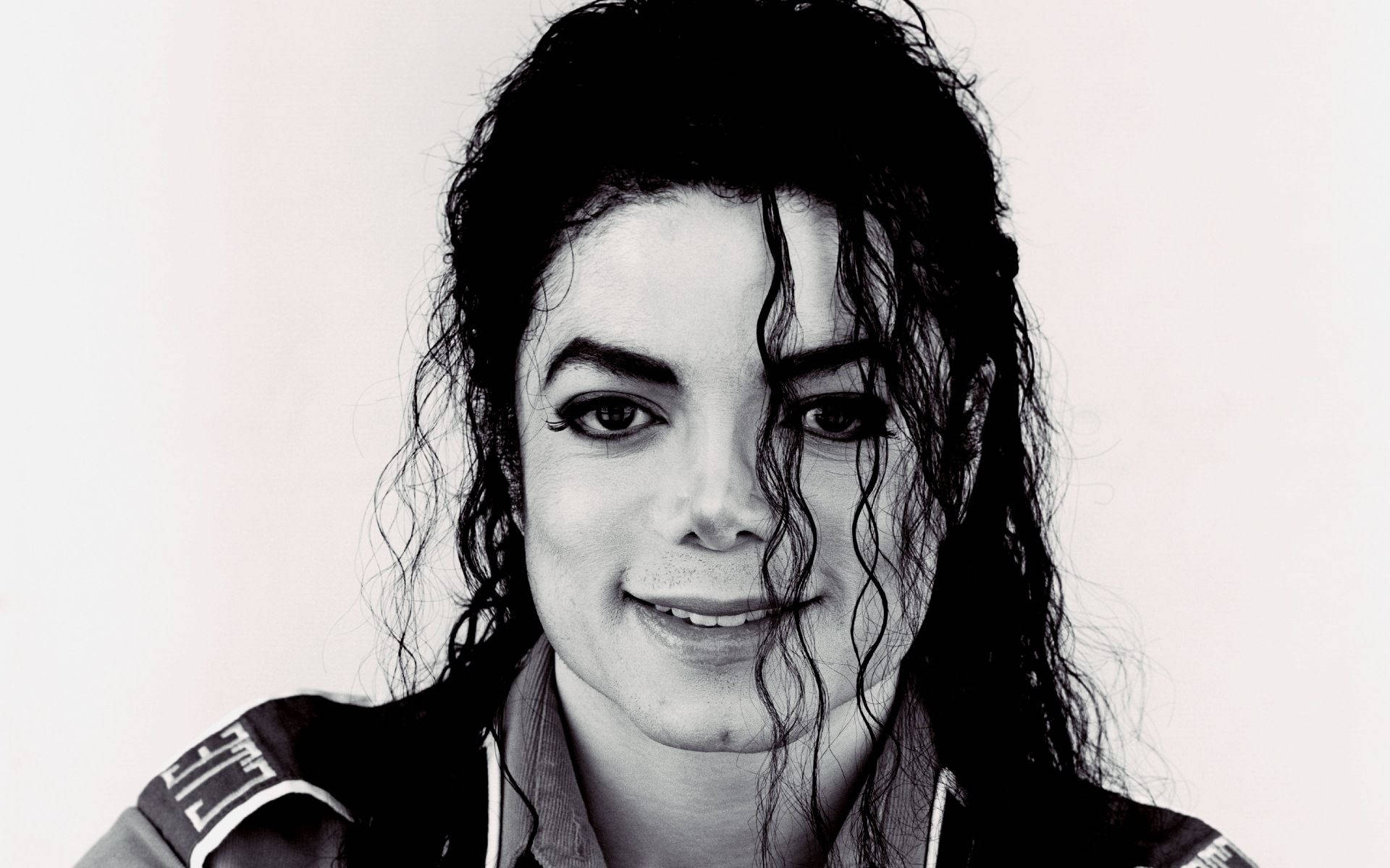 michael 桌布 壁紙 — 麥可傑克森的黑白肖像，濕曲髮，在純色背景前溫柔微笑。