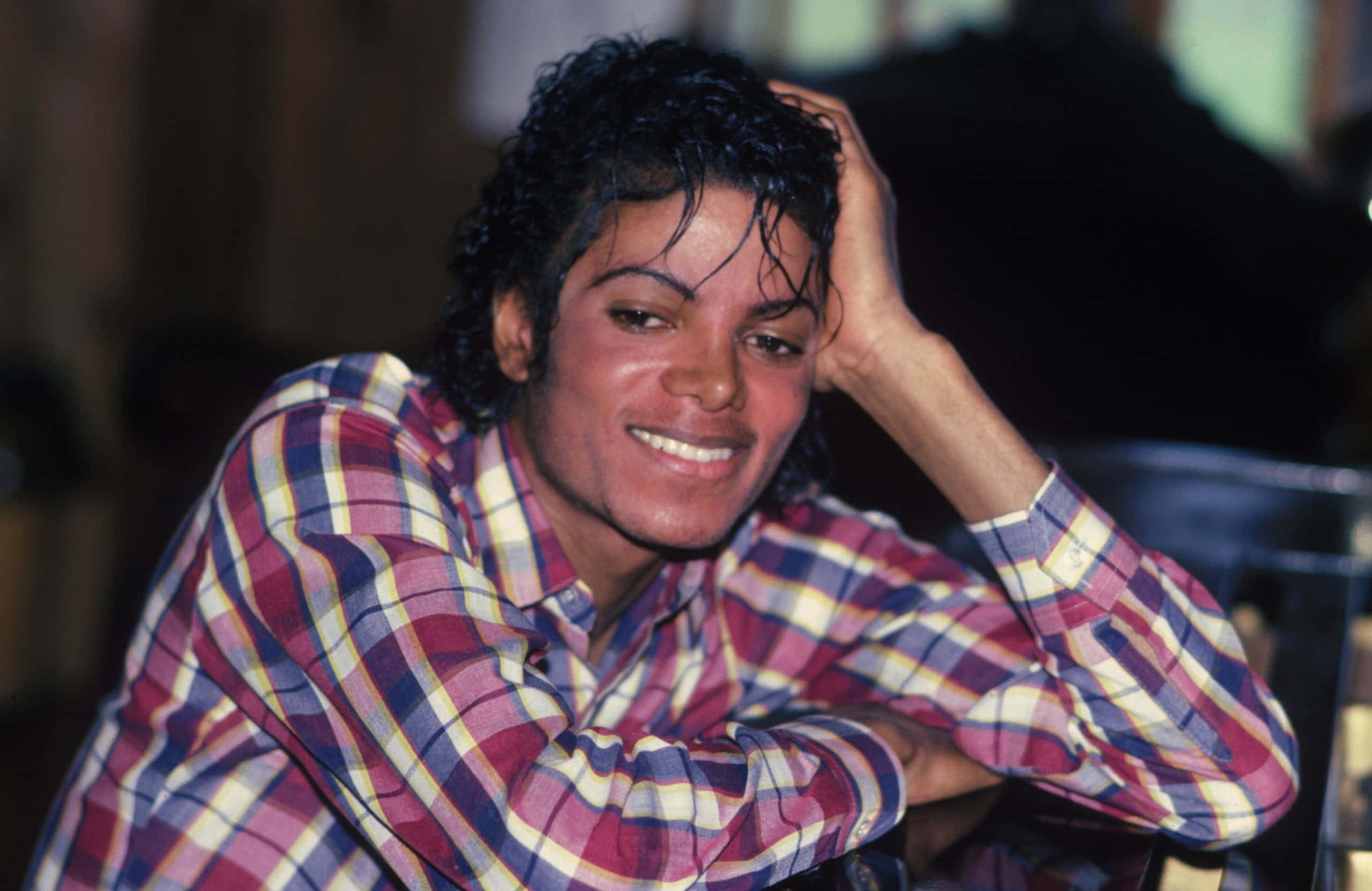 Young Michael Jackson 桌布 壁紙 — 麥可傑克森穿著格紋襯衫，將頭靠在手上，溫暖地微笑。
