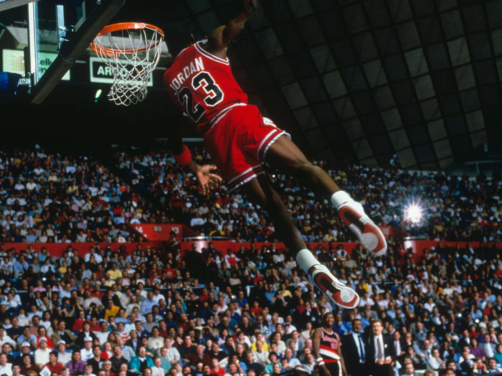 Jordan 桌布 壁紙 — 麥可喬丹在傳奇灌籃中，身穿標誌性紅色23號球衣，在擠滿觀眾的籃球場上空翱翔。