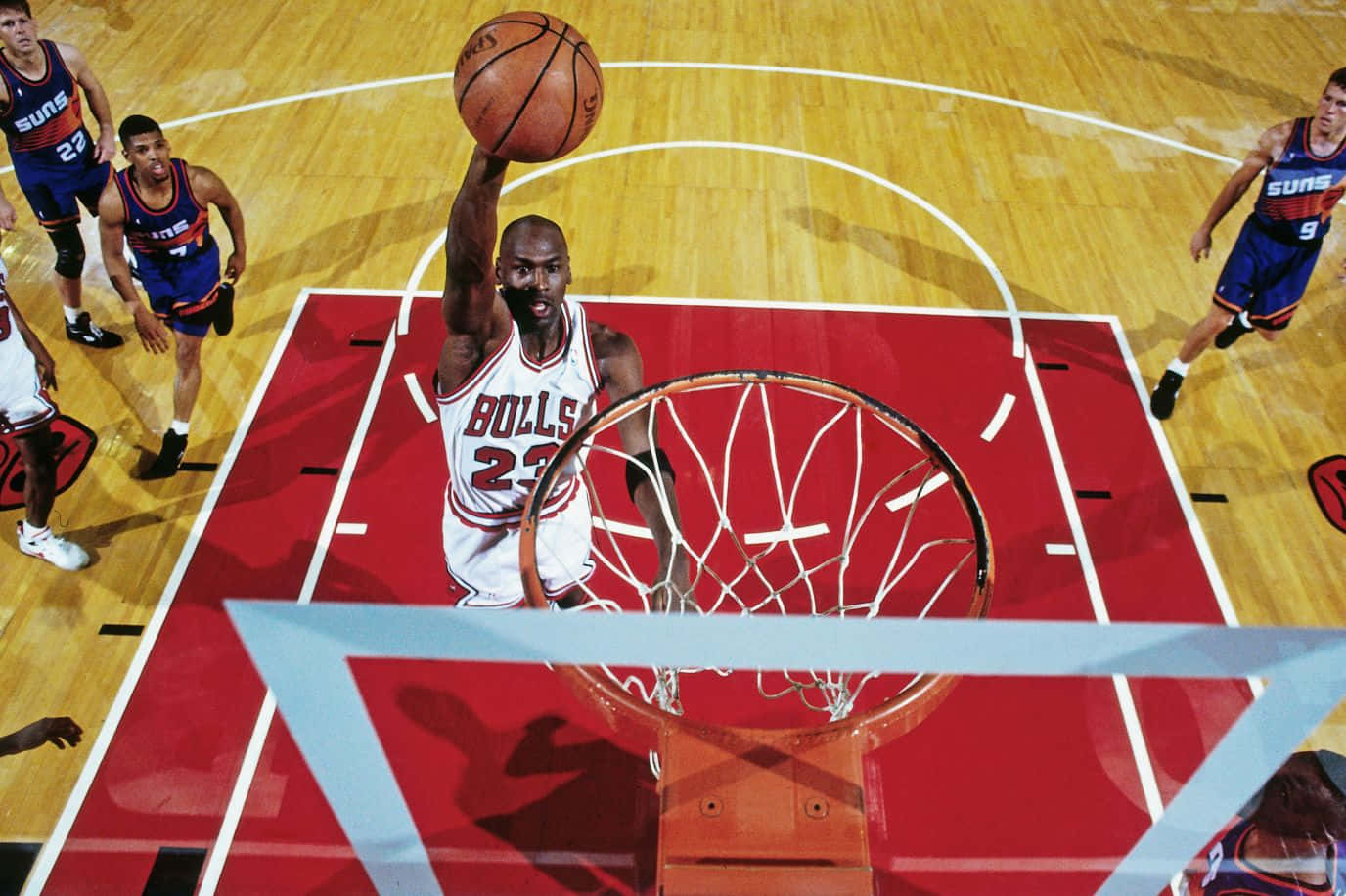 Jordan 桌布 壁紙 — 麥可喬丹在對陣太陽隊的比賽中，身穿公牛隊球衣，在籃框上方飛翔，完成一次強力灌籃。