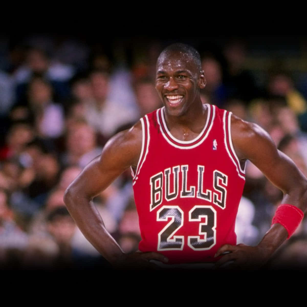 Jordan 桌布 壁紙 — 麥可喬丹在比賽中自信地微笑，身穿標誌性的紅色公牛隊23號球衣，雙手叉腰。