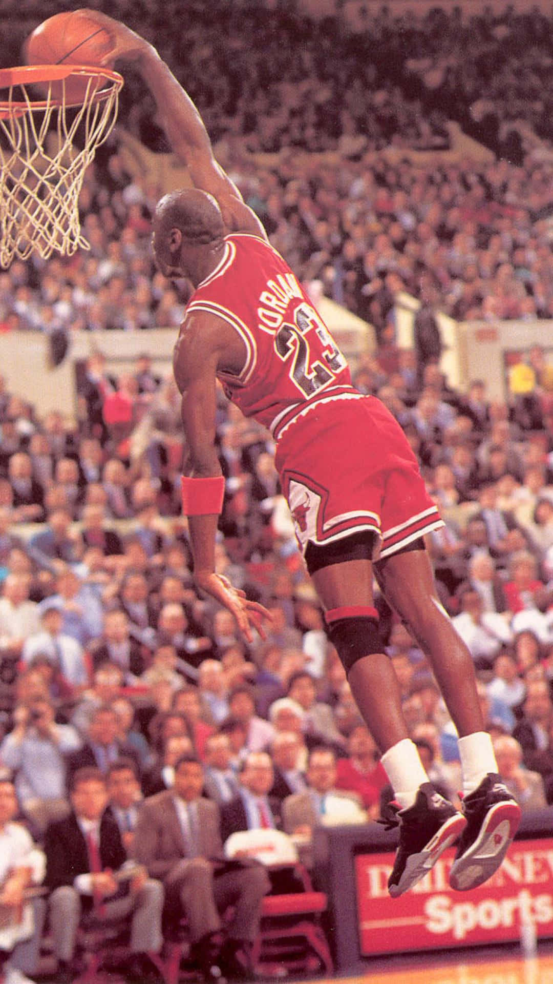 Jordan 桌布 壁紙 — 麥可喬丹穿著標誌性的紅色球衣在空中翱翔，在擠滿觀眾的場館上扣籃。