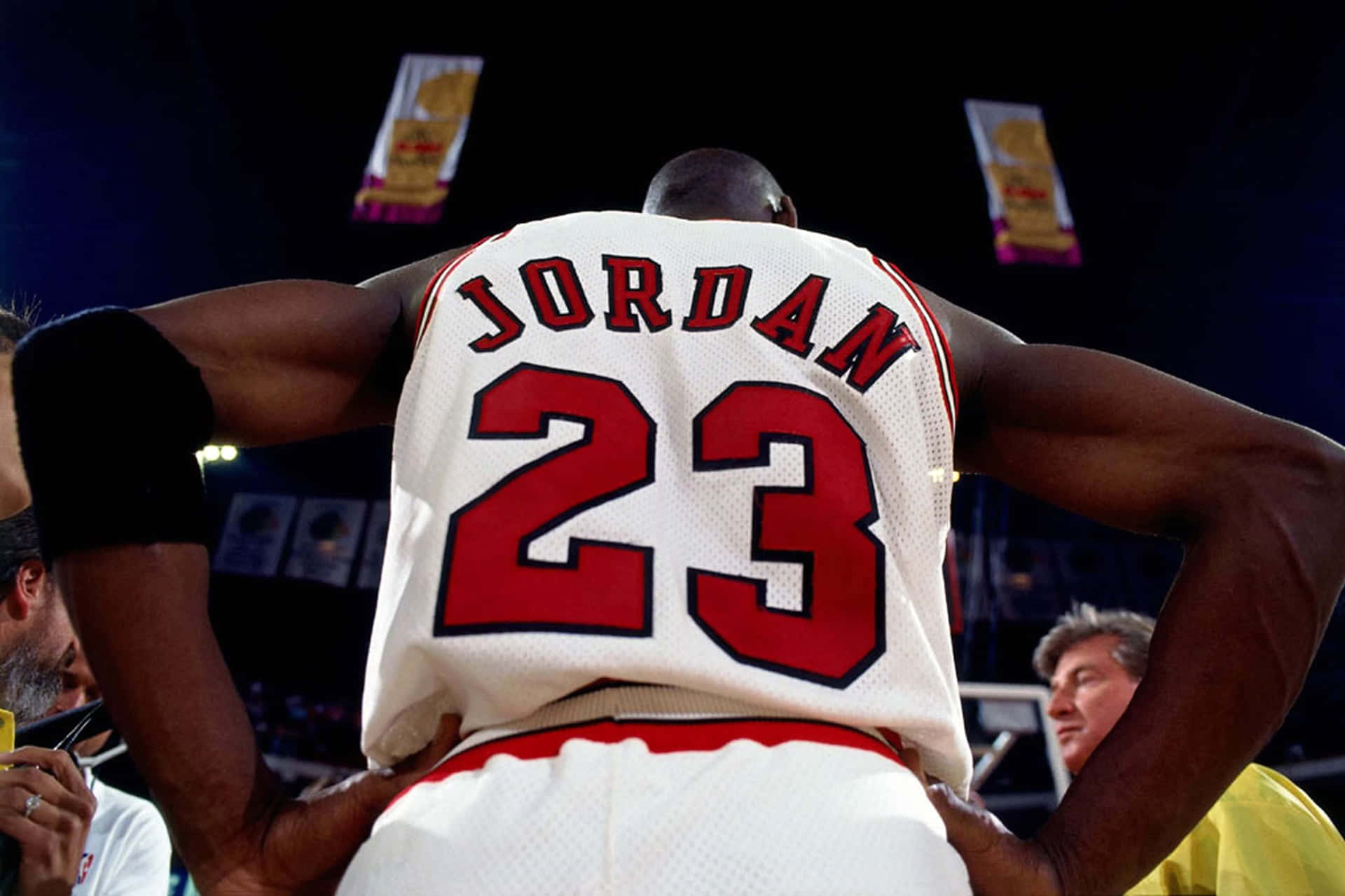 NBA 桌布 壁紙 — 麥可喬丹身穿白色23號球衣，在場館燈光下舉起雙臂站在球場上的背面視角。