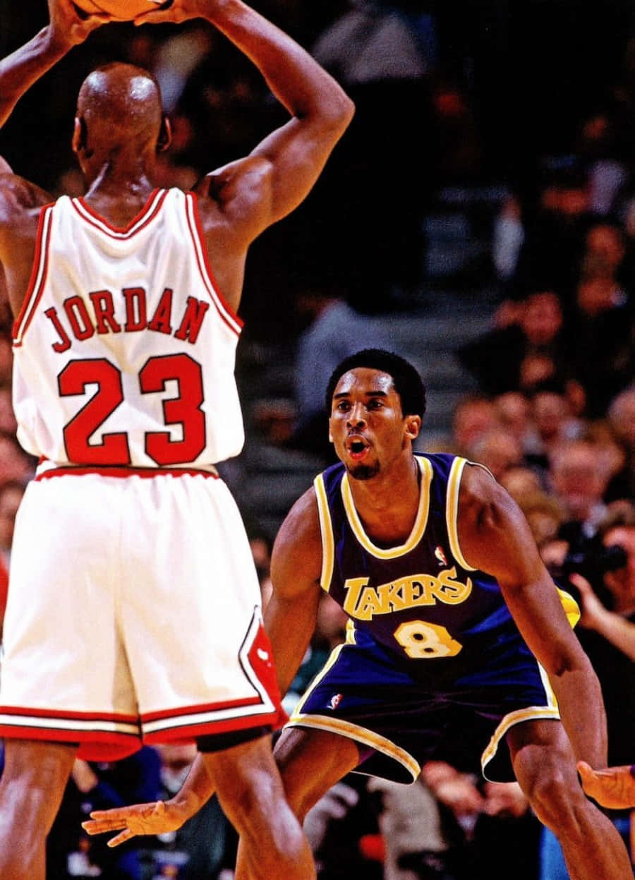 Kobe Bryant And Michael Jordan 桌布 壁紙 — 麥可喬丹身穿白色球衣跳起投籃，而柯比布萊恩身穿紫色湖人球衣在擠滿人的球場上激烈防守。