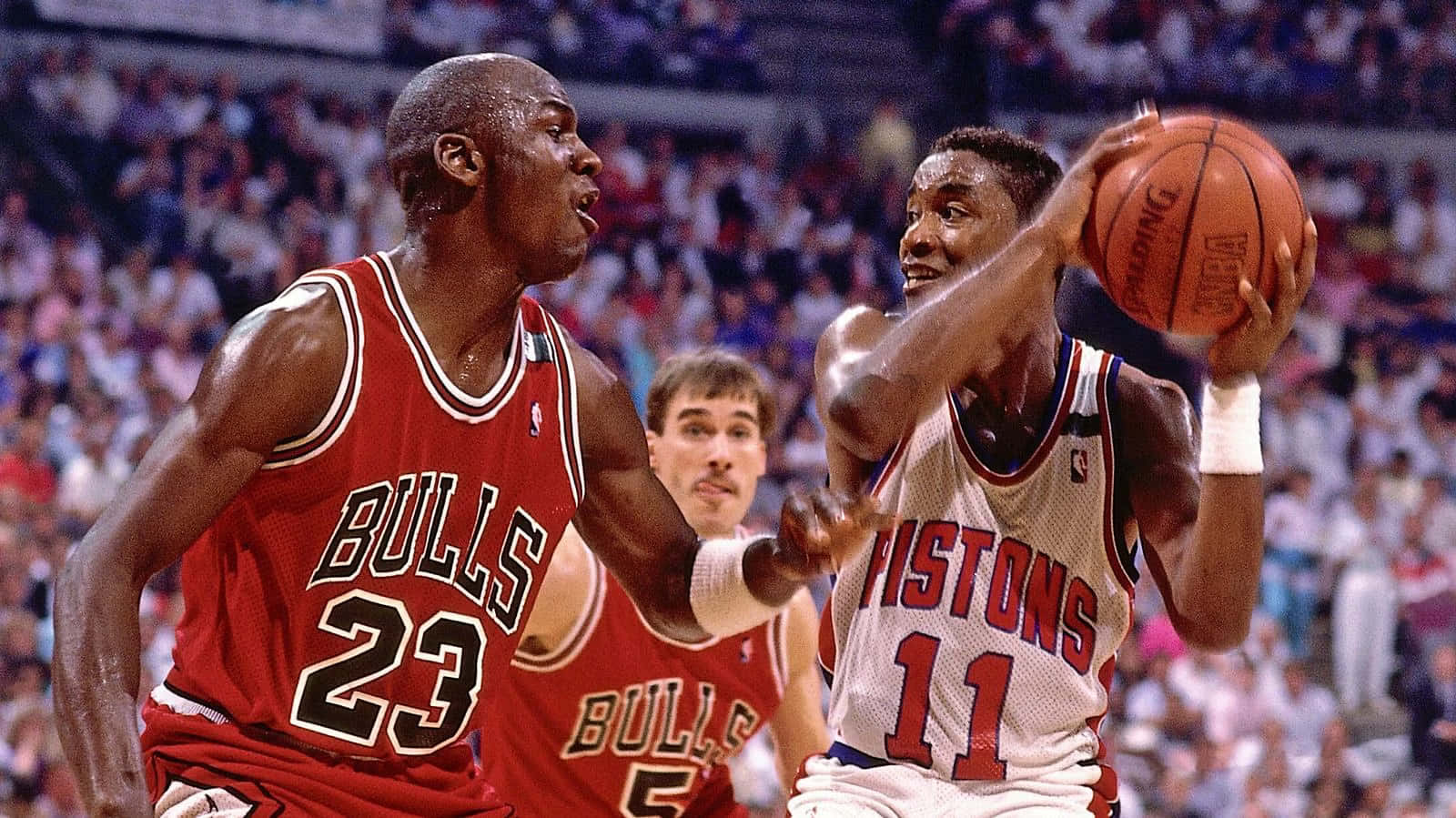 NBA 桌布 壁紙 — 麥可喬丹身穿紅色公牛球衣，在擠滿觀眾的球場上，積極防守身穿活塞球衣的伊西亞·托馬斯投籃。