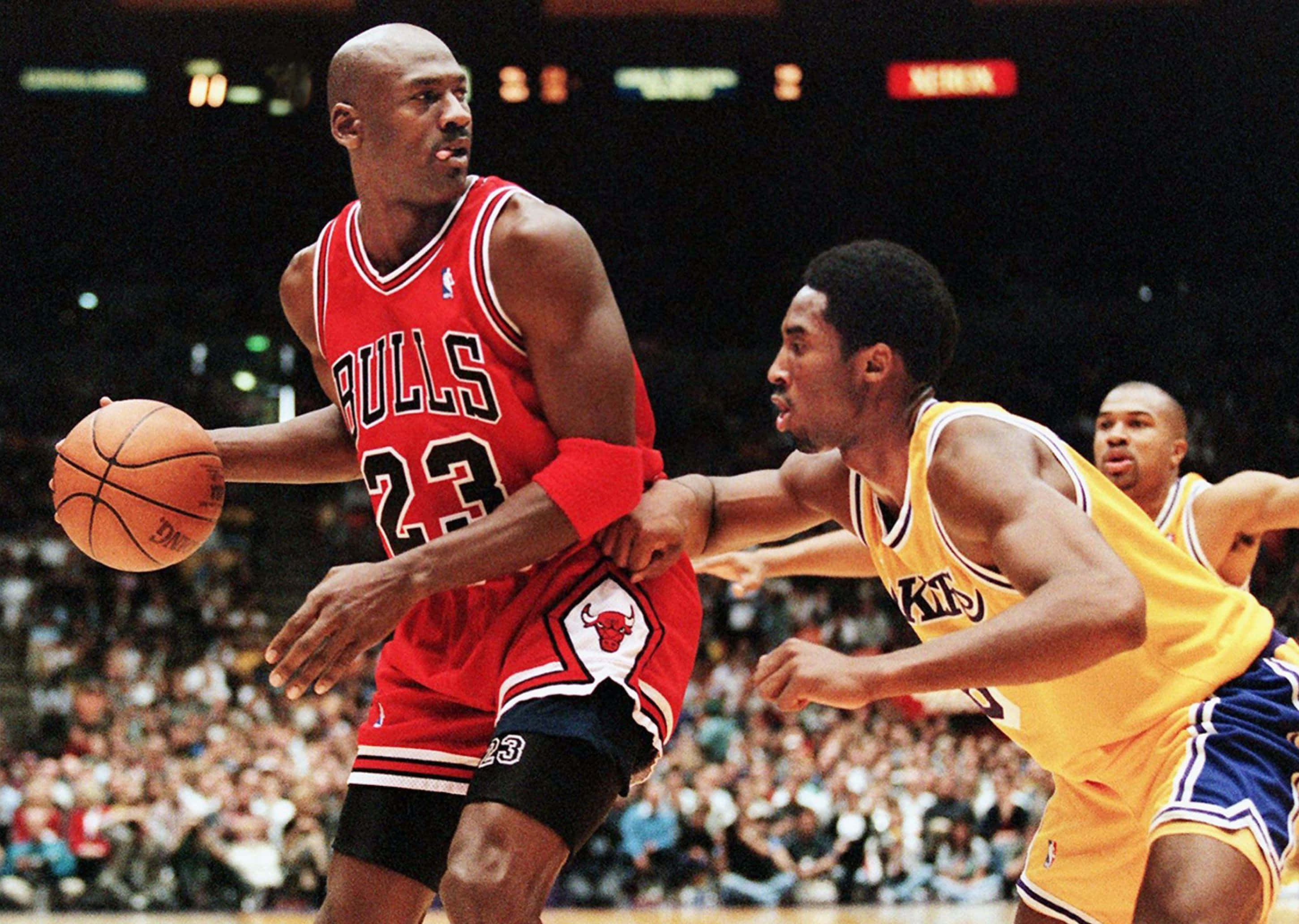 Jordan And Kobe 桌布 壁紙 — 麥可喬丹身穿紅色公牛球衣，在明亮的場館燈光下進行激烈的籃球比賽，運球越過一名身穿黃色球衣的防守球員。