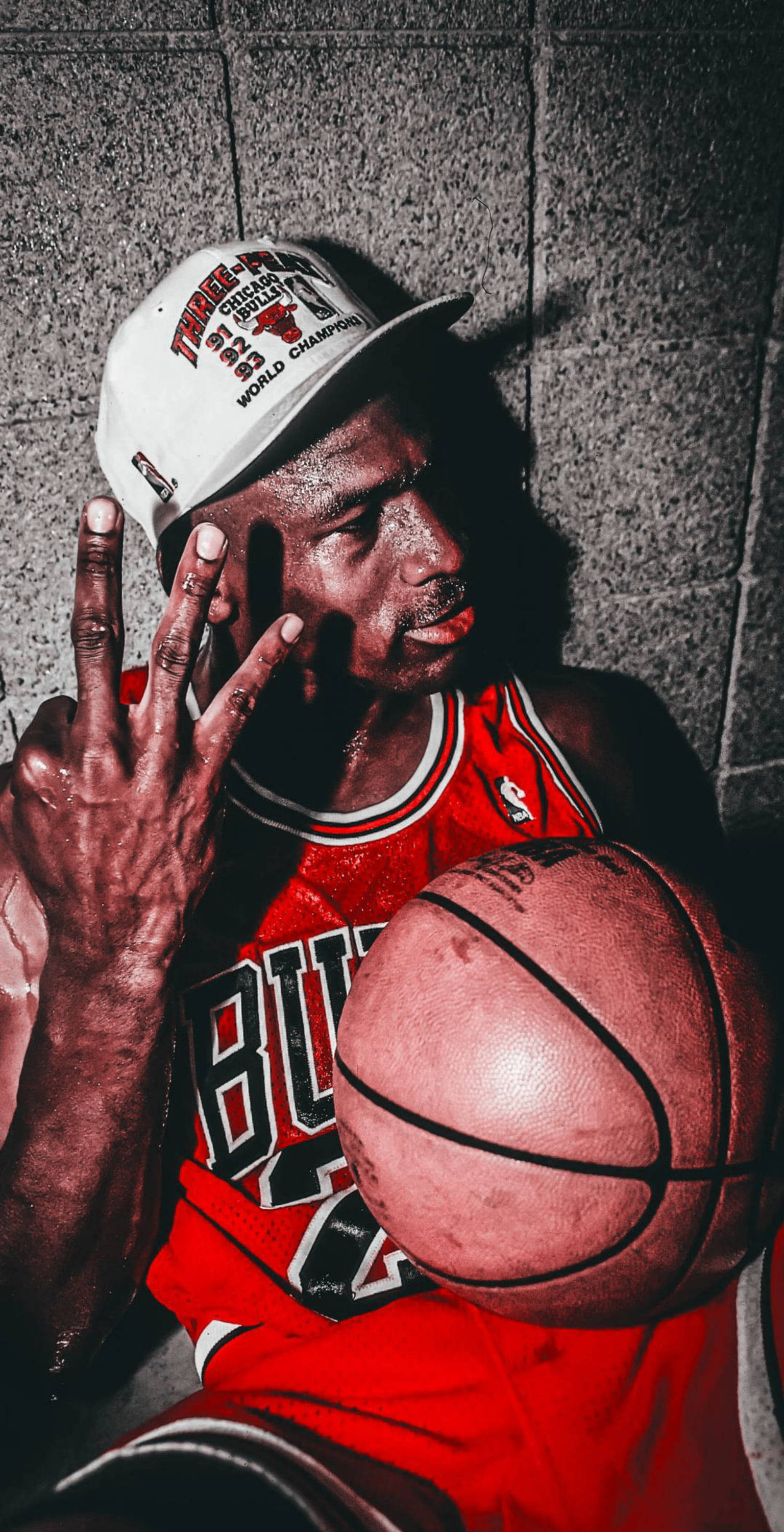 籃球 Jordan 桌布 壁紙 — 麥可喬丹身穿紅色公牛隊球衣，手持籃球，在粗糙的混凝土牆前伸出三根手指。