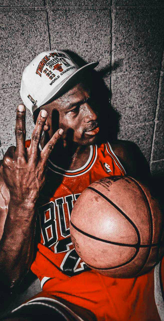 NBA 桌布 壁紙 — 麥可喬丹身穿紅色公牛隊球衣，靠著混凝土牆，手持籃球並豎起兩根手指。