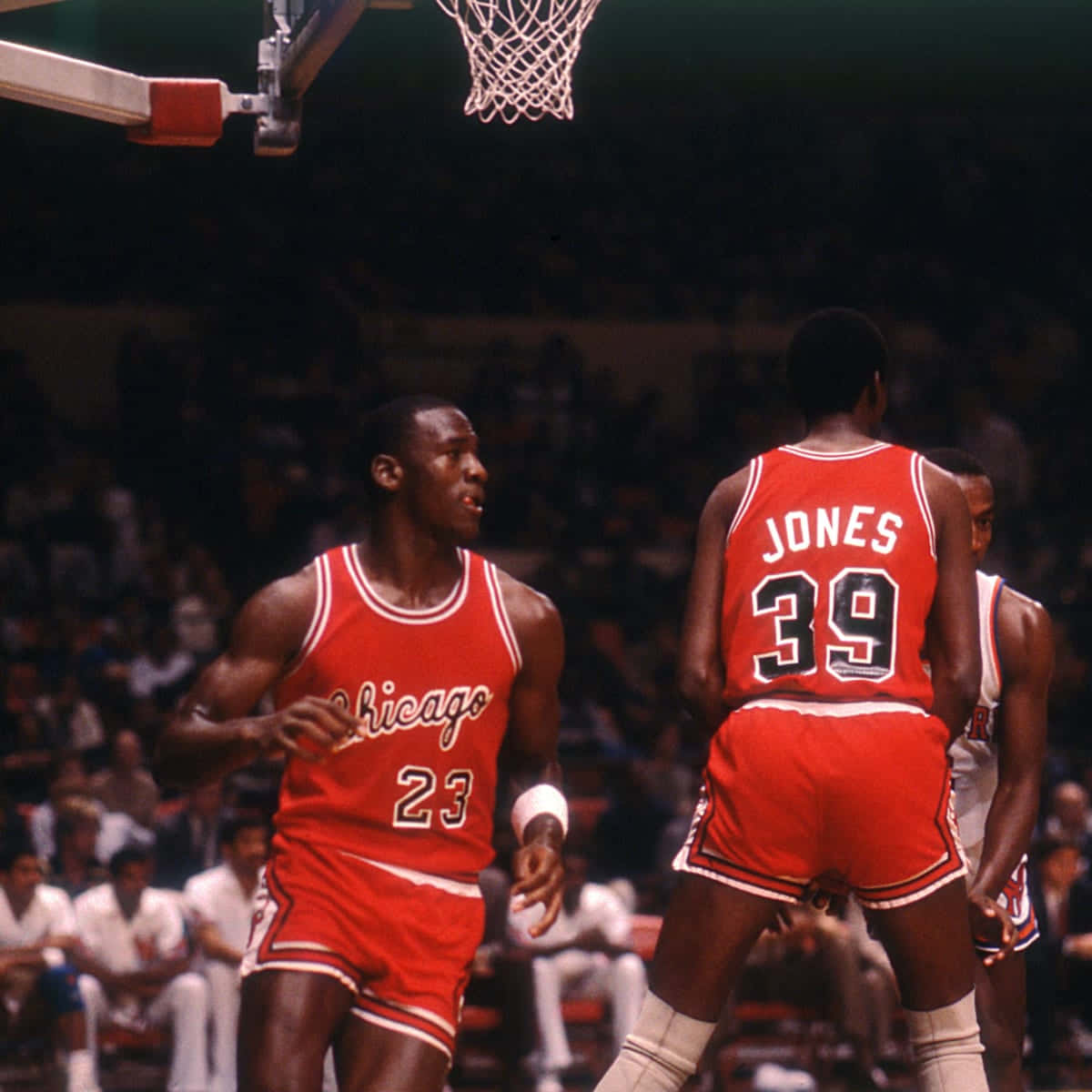 Jordan 桌布 壁紙 — 麥可喬丹身穿紅色芝加哥公牛隊23號球衣，在明亮的場館燈光下，與隊友39號瓊斯防守時運球進行籃球比賽。