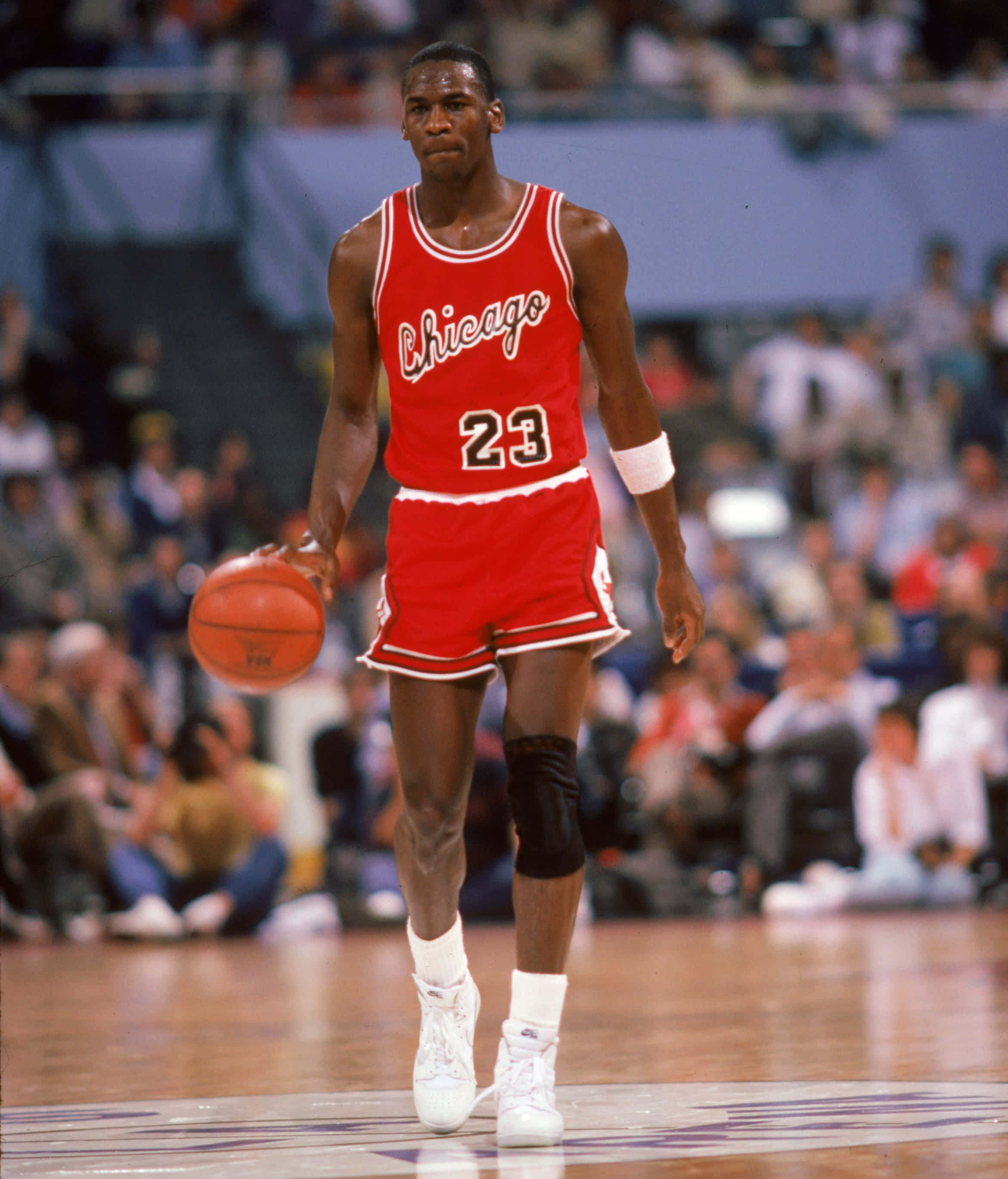 Jordan 桌布 壁紙 — 麥可喬丹身穿紅色芝加哥公牛隊23號球衣，在硬木地板上運球，背景有模糊的觀眾。