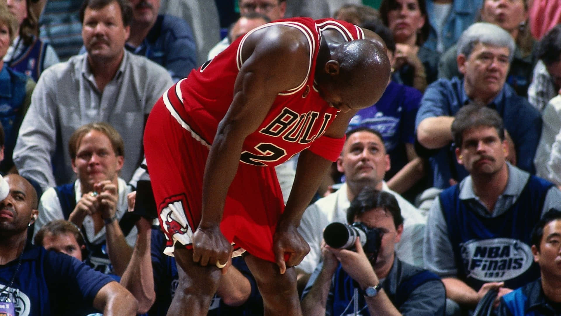 Jordan 桌布 壁紙 — 麥可喬丹身穿紅色芝加哥公牛隊球衣，在NBA總決賽比賽中彎腰向前，筋疲力盡，背景有觀眾。