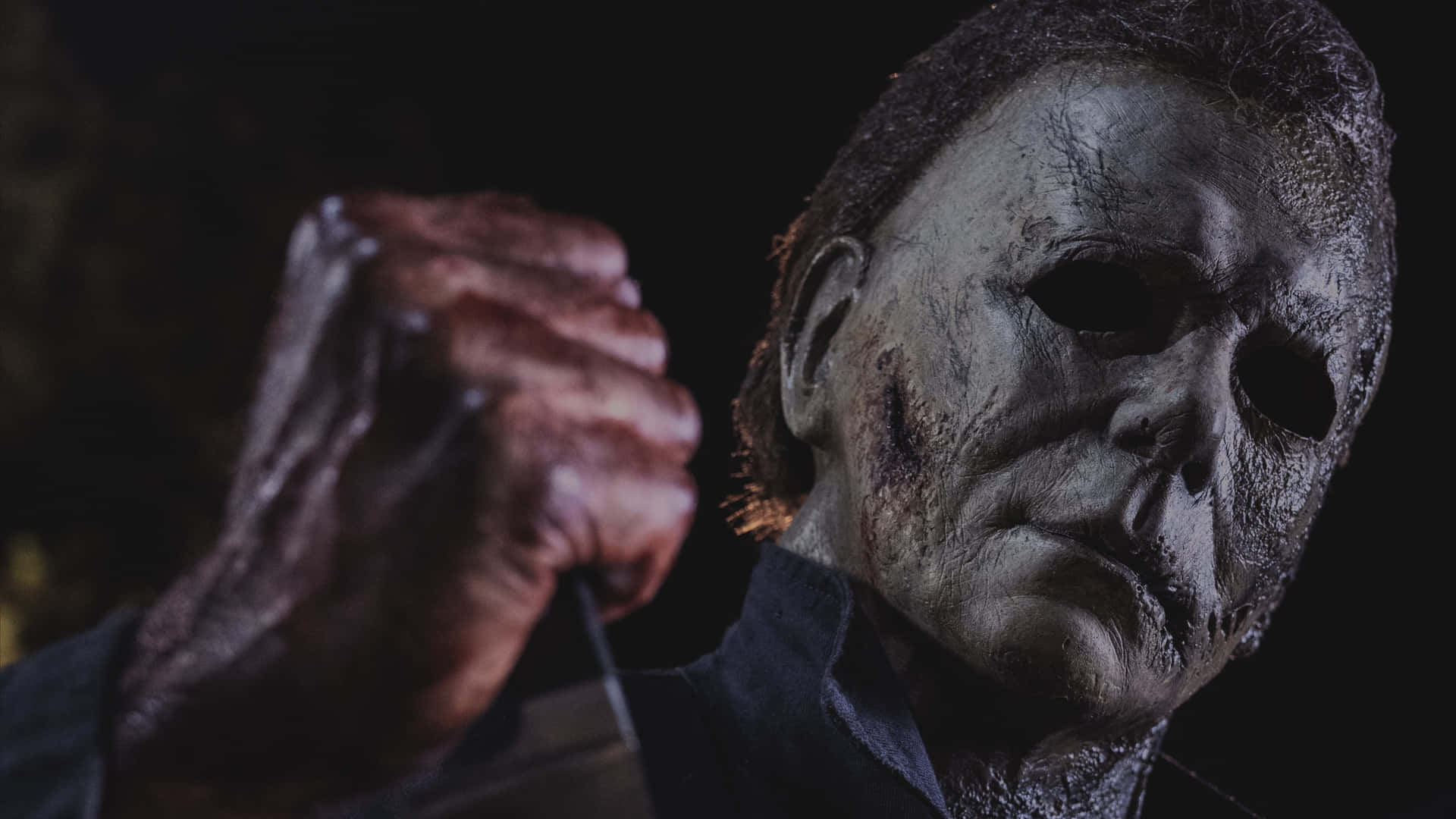 Michael Myers 桌布 壁紙 — 麥可邁爾斯近距離特寫，戴著標誌性白色面具，在黑暗背景下手持刀具。
