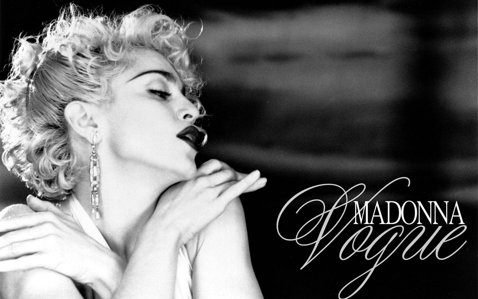 Madonna 桌布 壁紙 — 麥當娜在模糊背景前擺姿勢的戲劇性黑白肖像，捲髮和鮮明嘴唇。