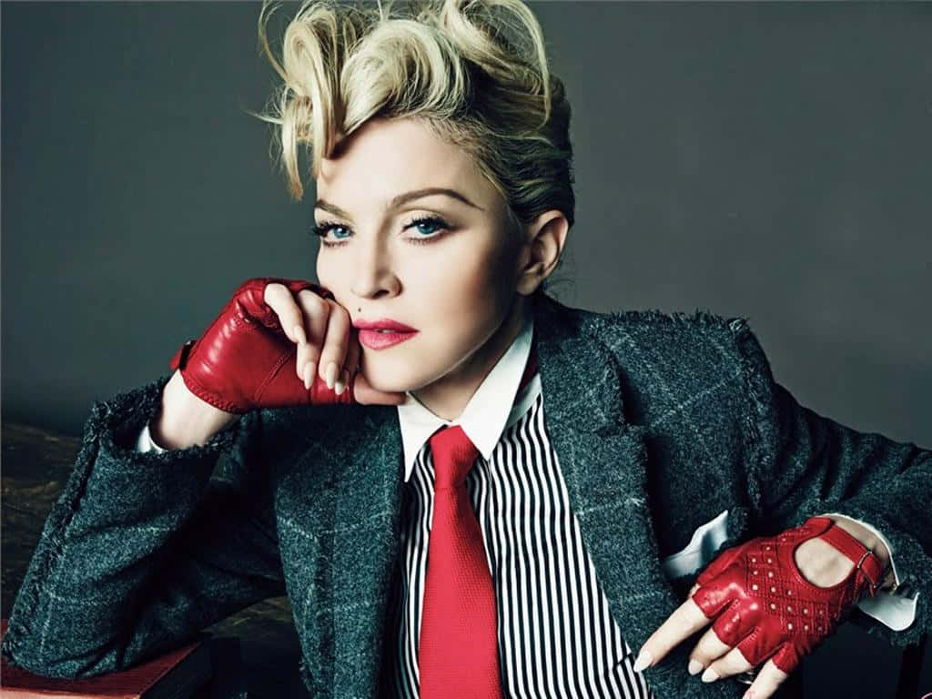 Madonna 桌布 壁紙 — 麥當娜自信地擺姿勢，身穿深色粗花呢西裝外套、條紋襯衫、紅色領帶和紅色無指手套，背景為柔和的灰色。
