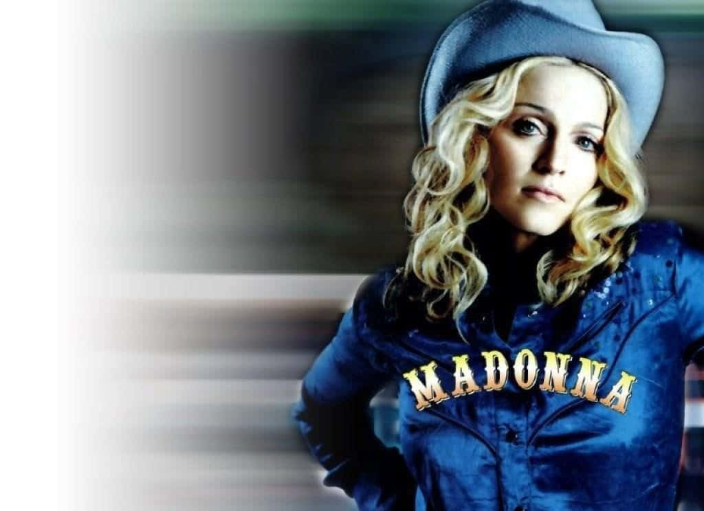 Madonna 桌布 壁紙 — 麥當娜身穿藍色牛仔外套和帽子，胸前繡有她的名字，在模糊的背景前凝視著。
