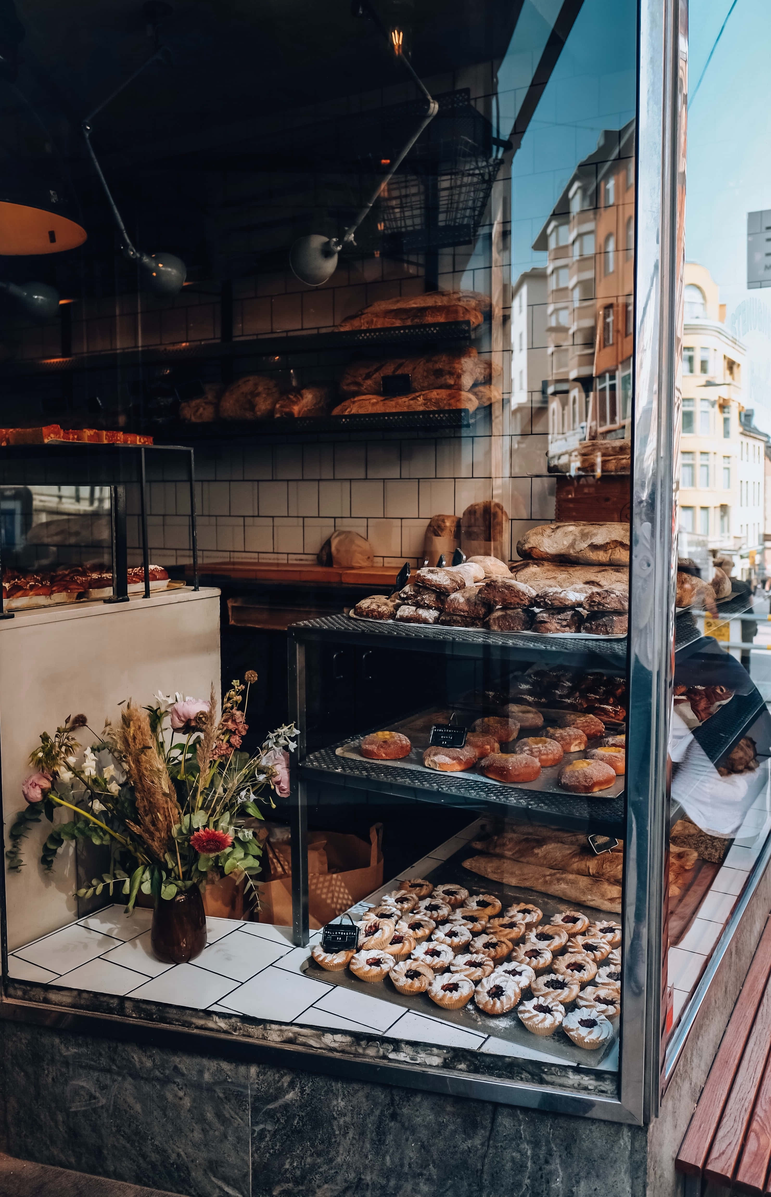 Bakery 桌布 壁紙 — 麵包店櫥窗展示糕點和麵包，配有花瓶和城市倒影。